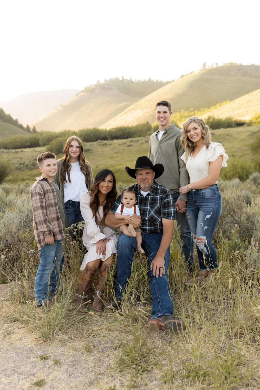 Candid family portrait with multiple generations gathered on mountainside during sunset.