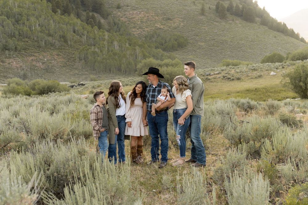 Family group walking together through sage brush on a mountainside at sunset.