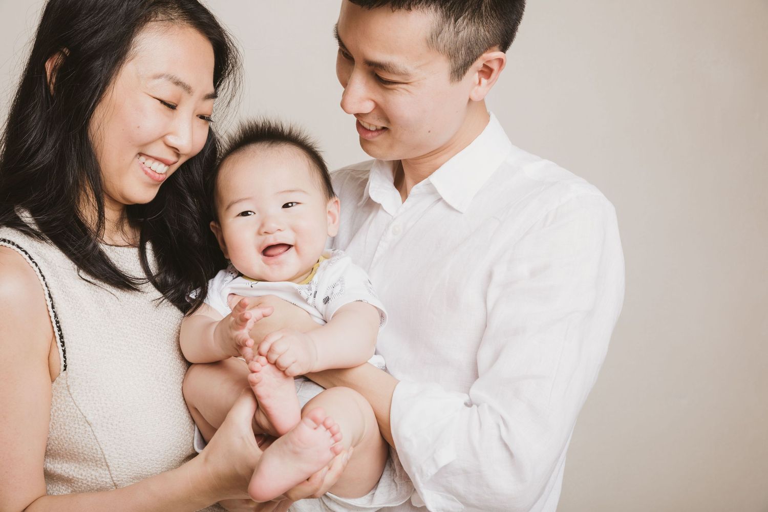 Intimate family portrait against neutral background showing tender moment with baby.