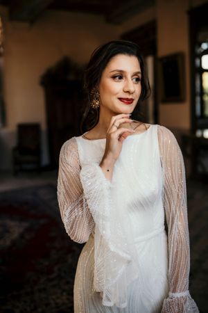 Elegant bridal portrait featuring a white lace long-sleeve wedding gown and statement earrings.