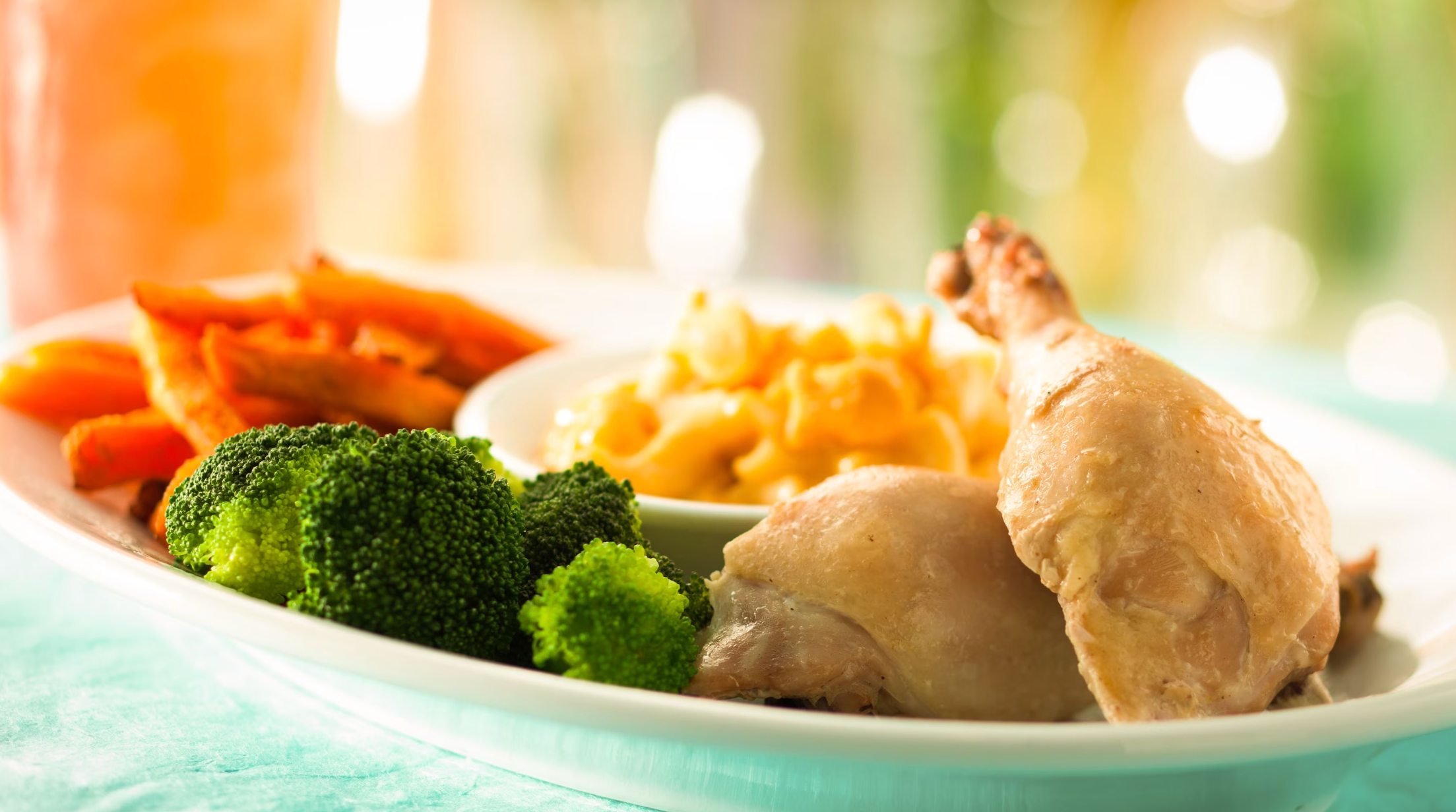 Fresh dinner plate with steamed vegetables, broccoli, carrots and chicken served on turquoise tablecloth.