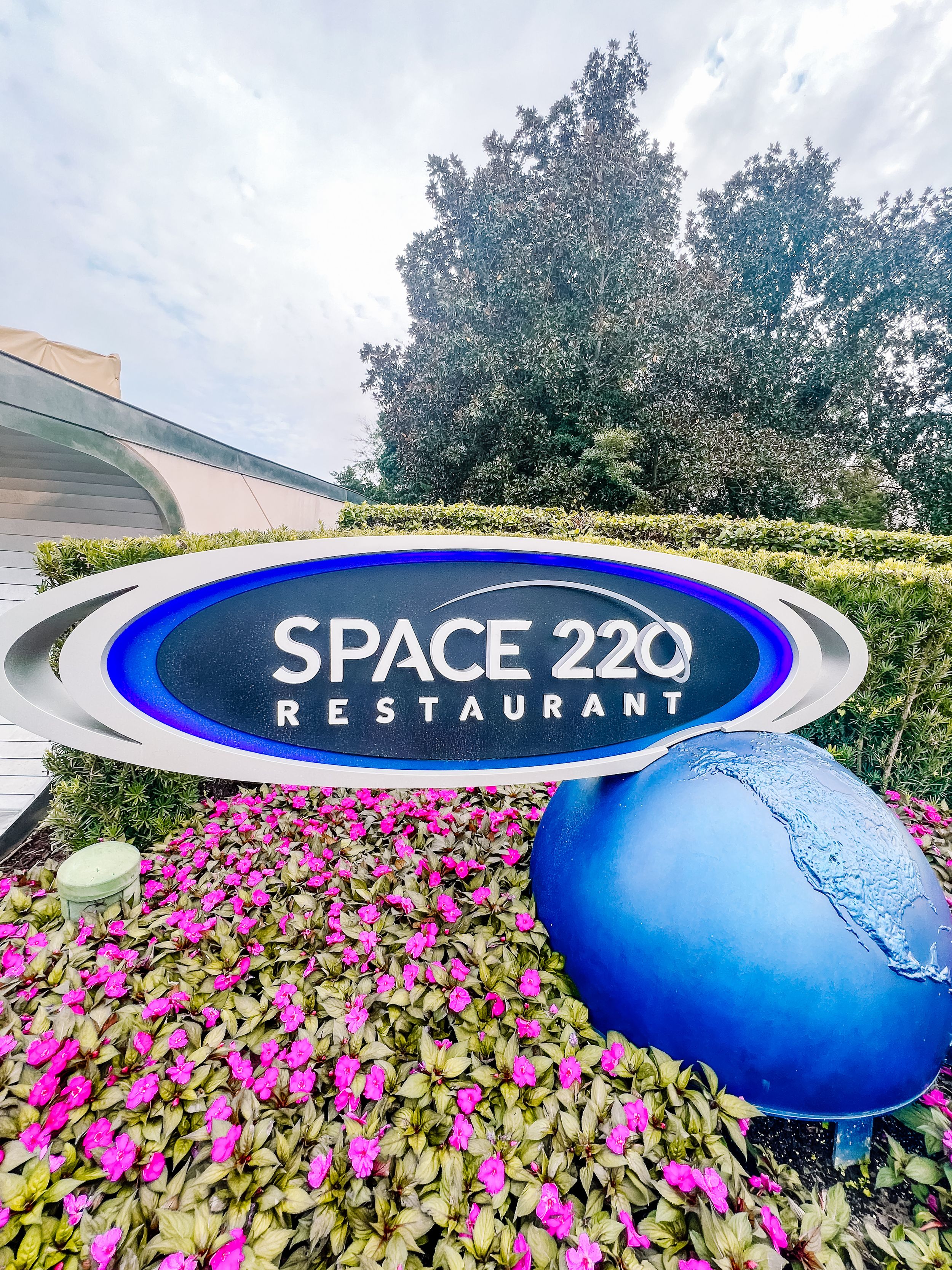 Close-up of Space 220 restaurant's oval logo with blue sphere decoration and flowering plants.