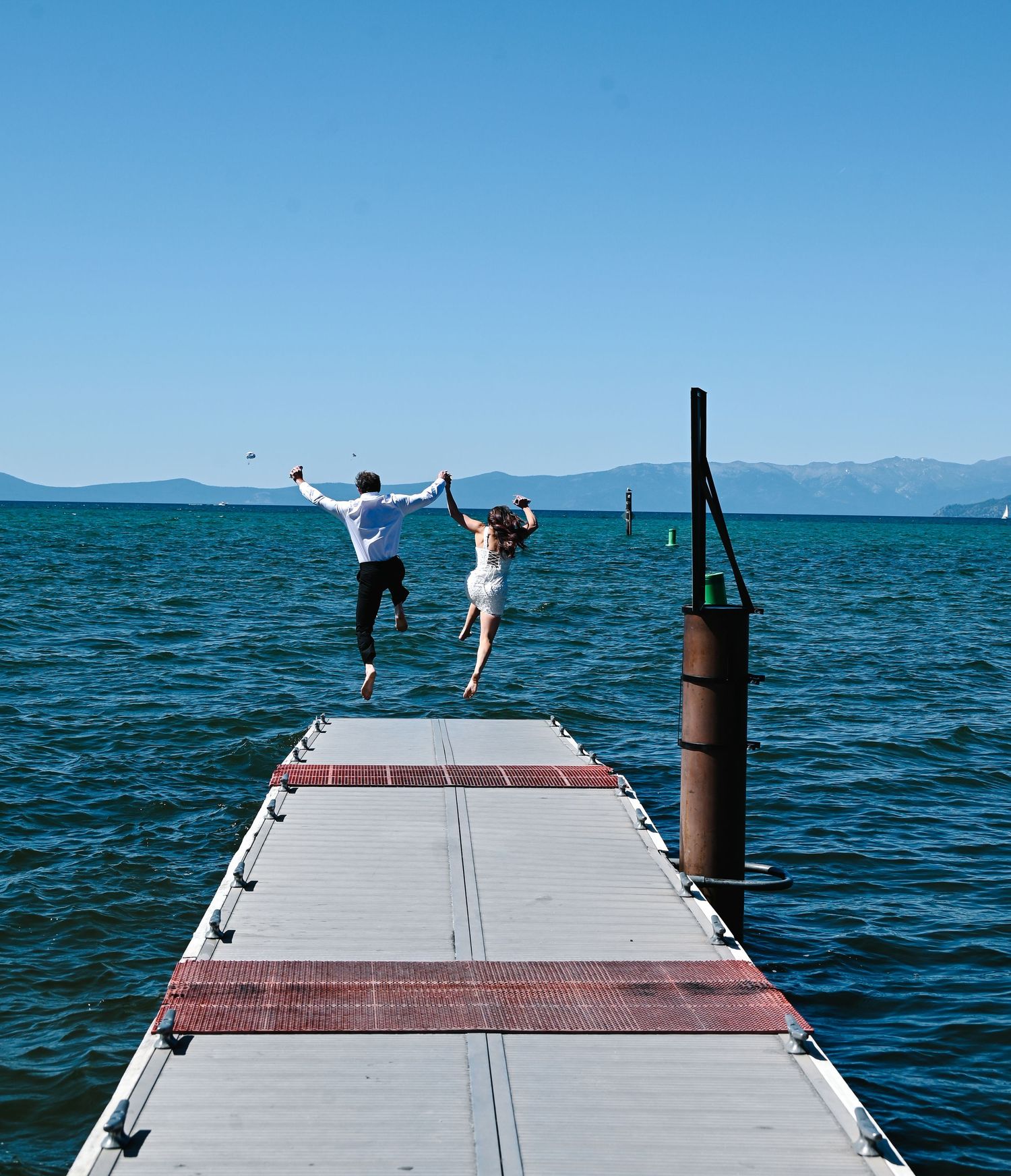 A sequential view of two people joyfully jumping off a wooden dock into blue ocean waters on a sunny day.
