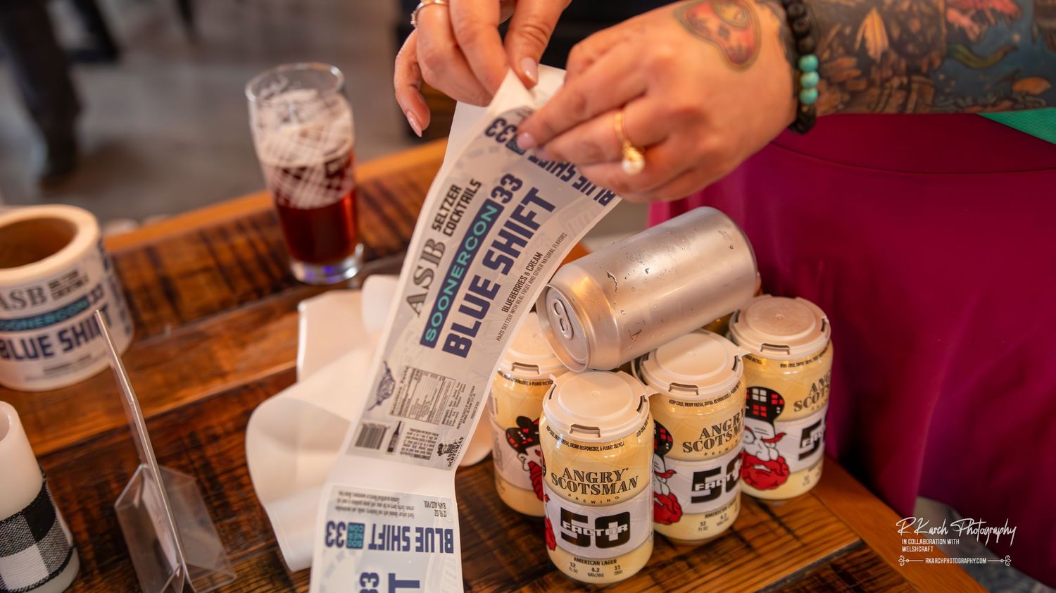 A lineup of craft beer bottles, ice cream containers, and Sooner Corn brand packaging displayed on a rustic wooden table.