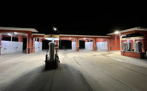 Empty gas station at night with illuminated fuel pumps and service bays visible under bright lighting.