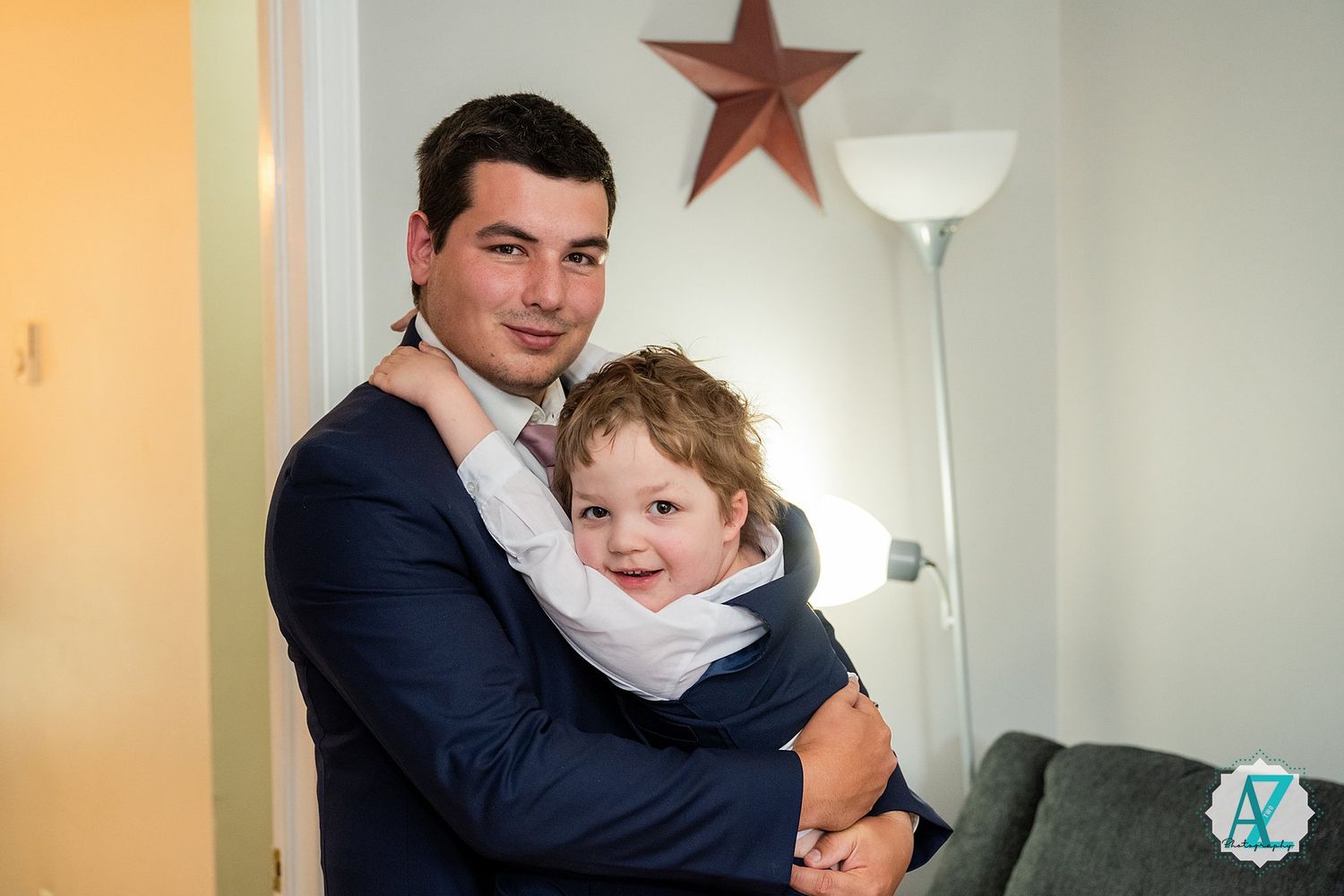 A person in a navy suit holds a young child in a light-colored outfit while standing in a room with a star decoration.