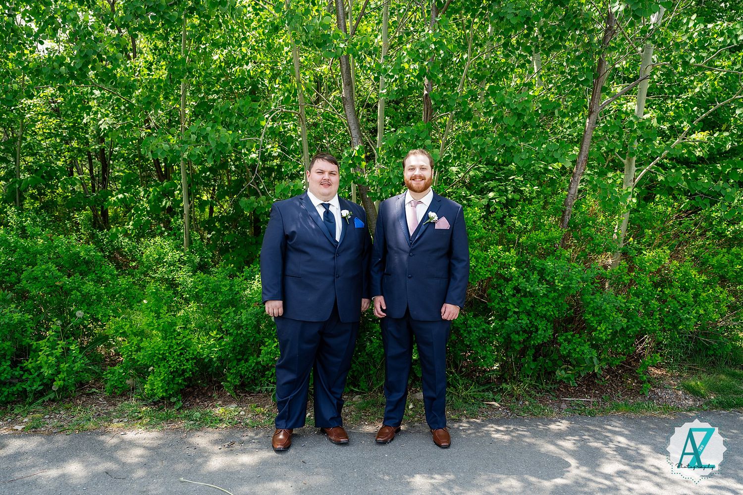 Two people in navy suits standing side by side on a path with lush green foliage in the background.