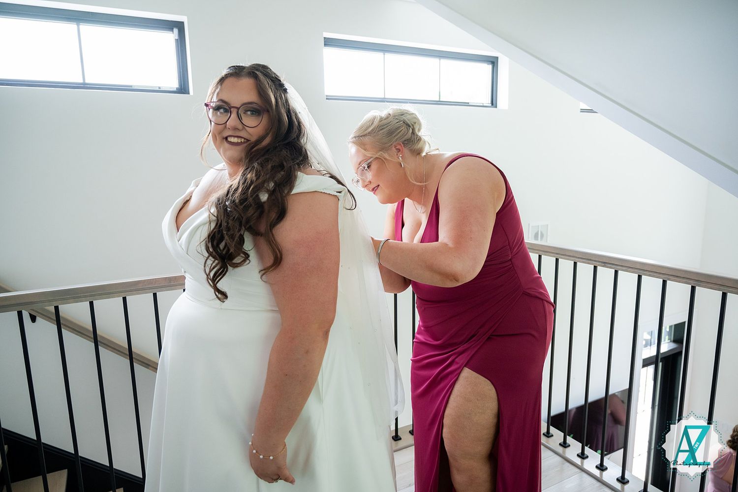 A person in a white wedding dress receives assistance with getting ready from someone wearing a deep pink dress.