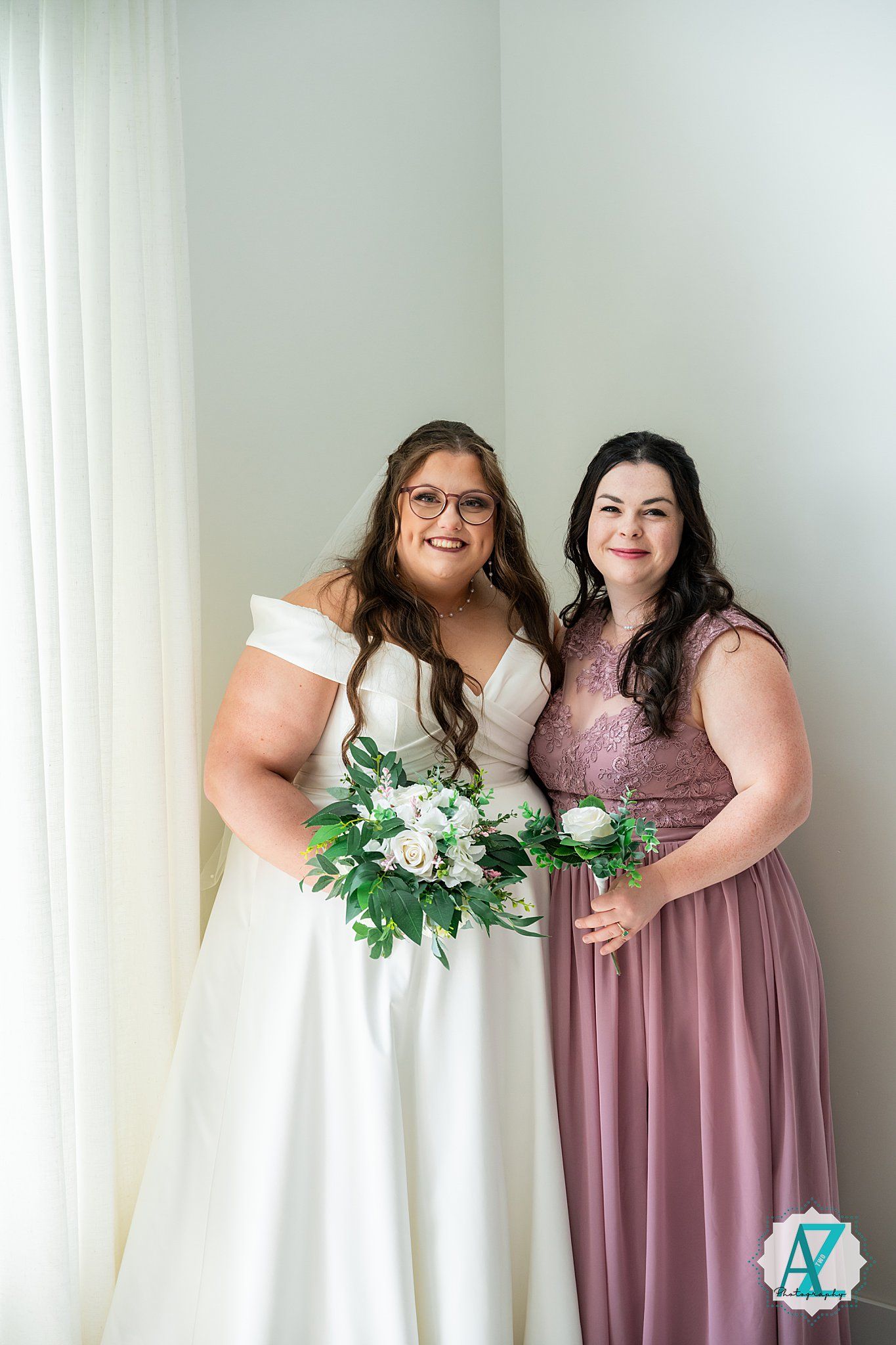 Two wedding party members share a joyful moment while holding elegant floral bouquets.