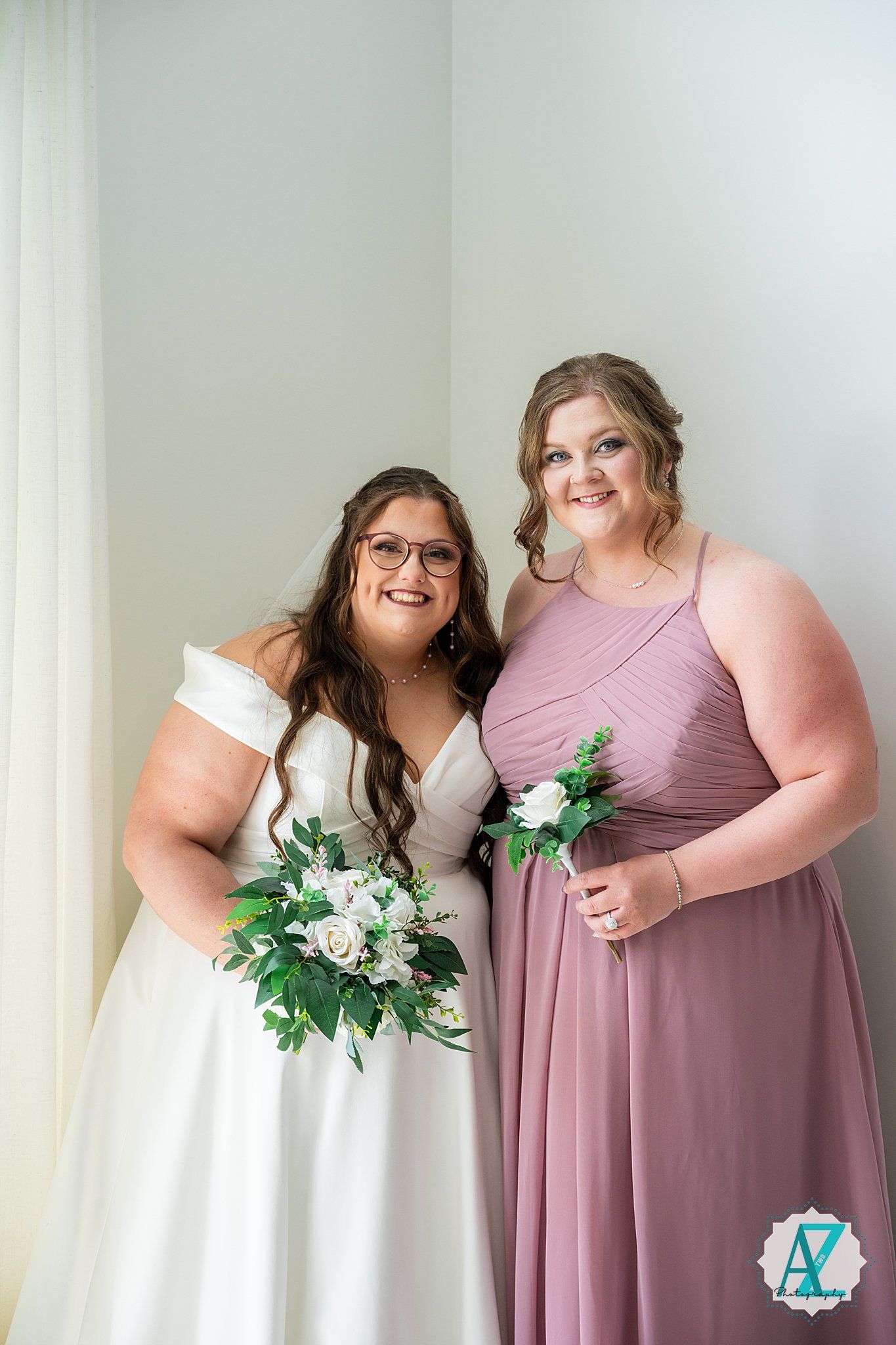 Two smiling figures pose together in wedding attire with white bridal gown and dusty rose bridesmaid dress.