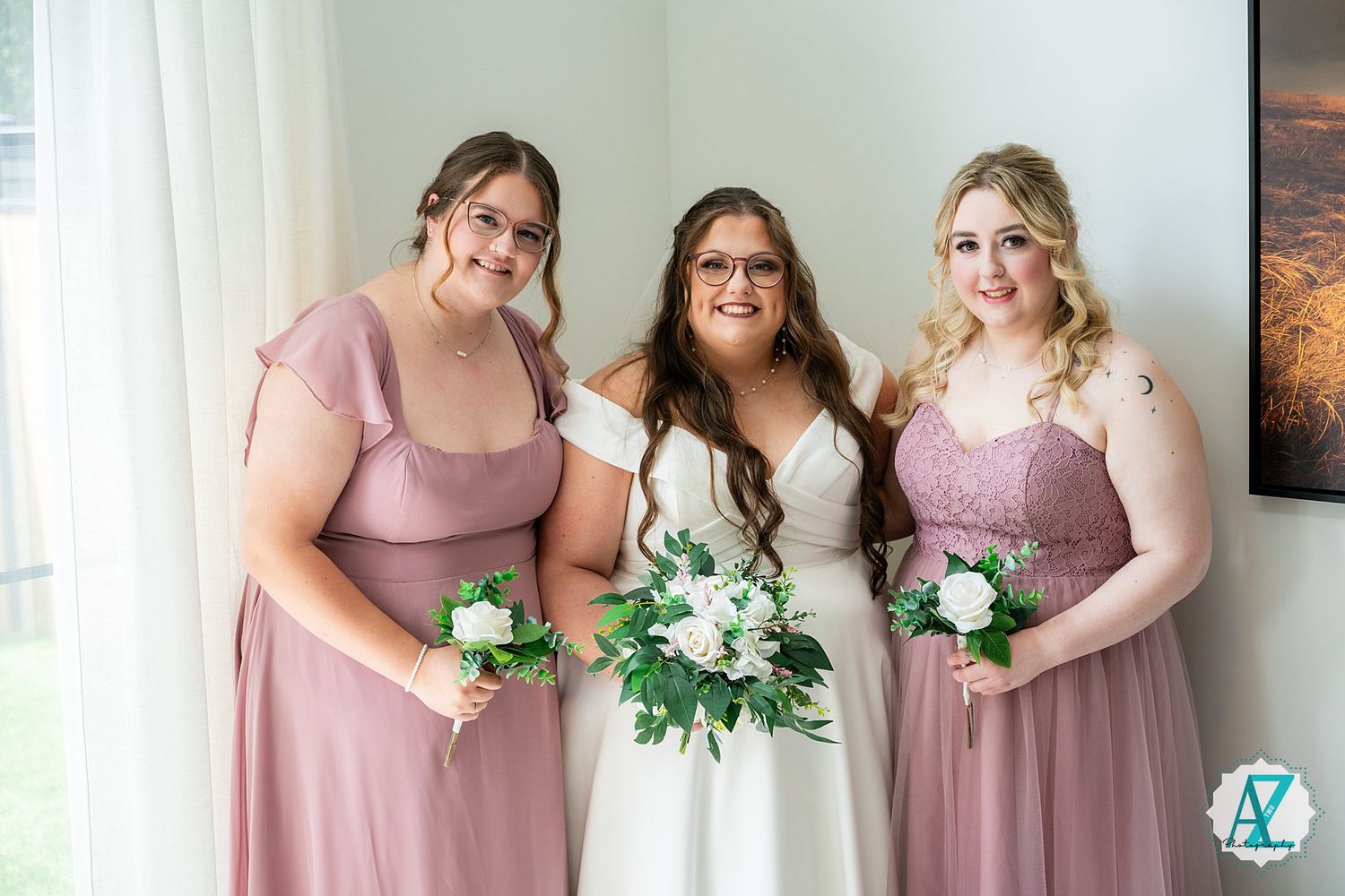 Wedding party poses together in matching mauve dresses while holding white floral bouquets.