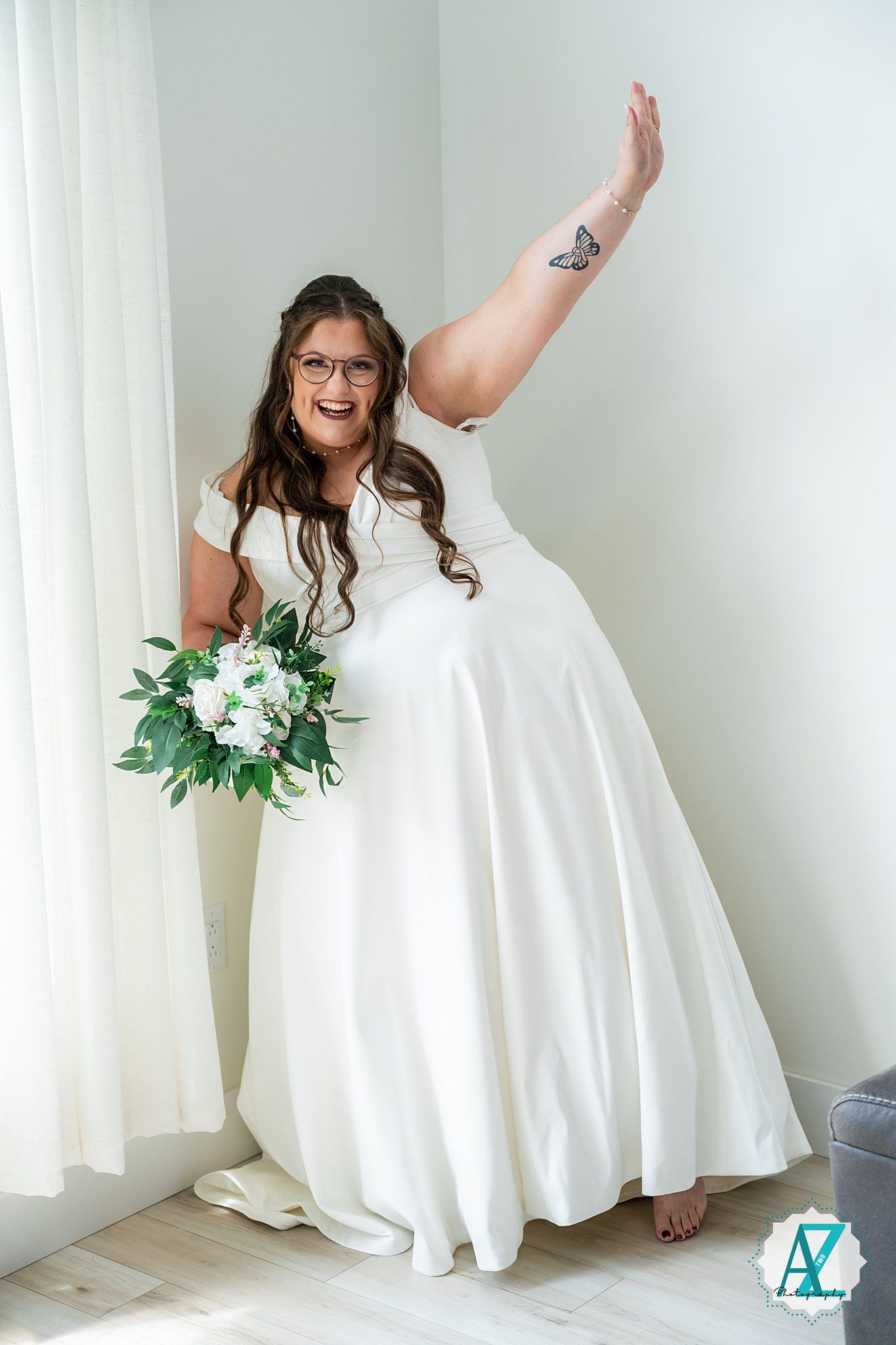 A bride in a flowing white wedding dress dances playfully in front of white curtains while holding a green bouquet.