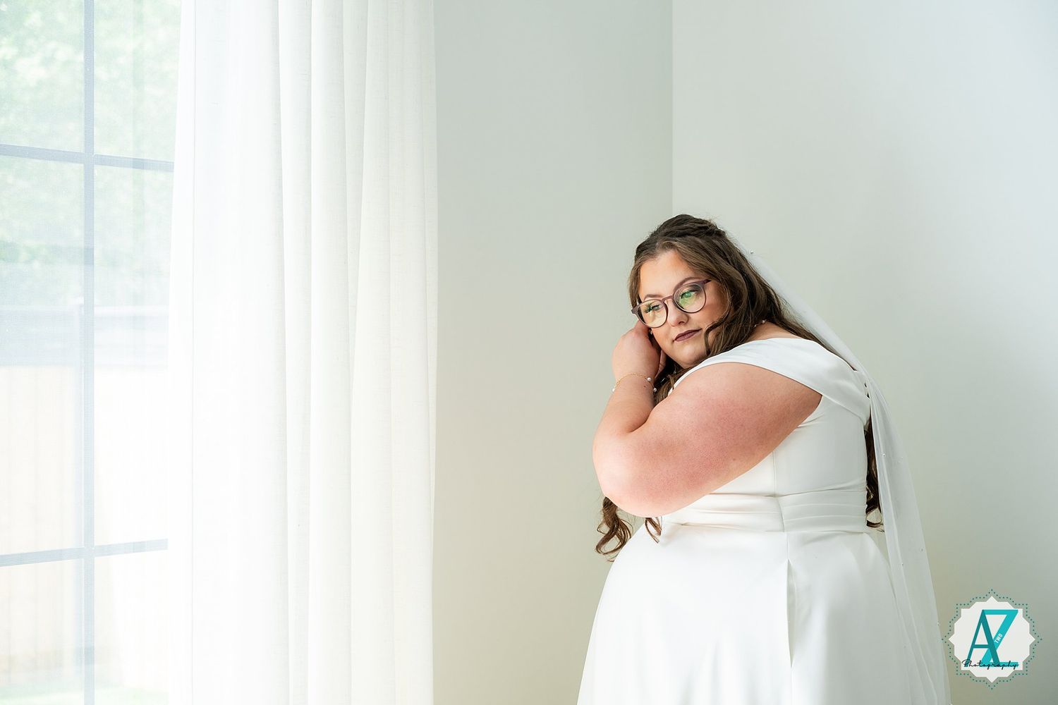Someone in a white dress hugs a pink pillow while sitting by a bright window in a minimalist room.