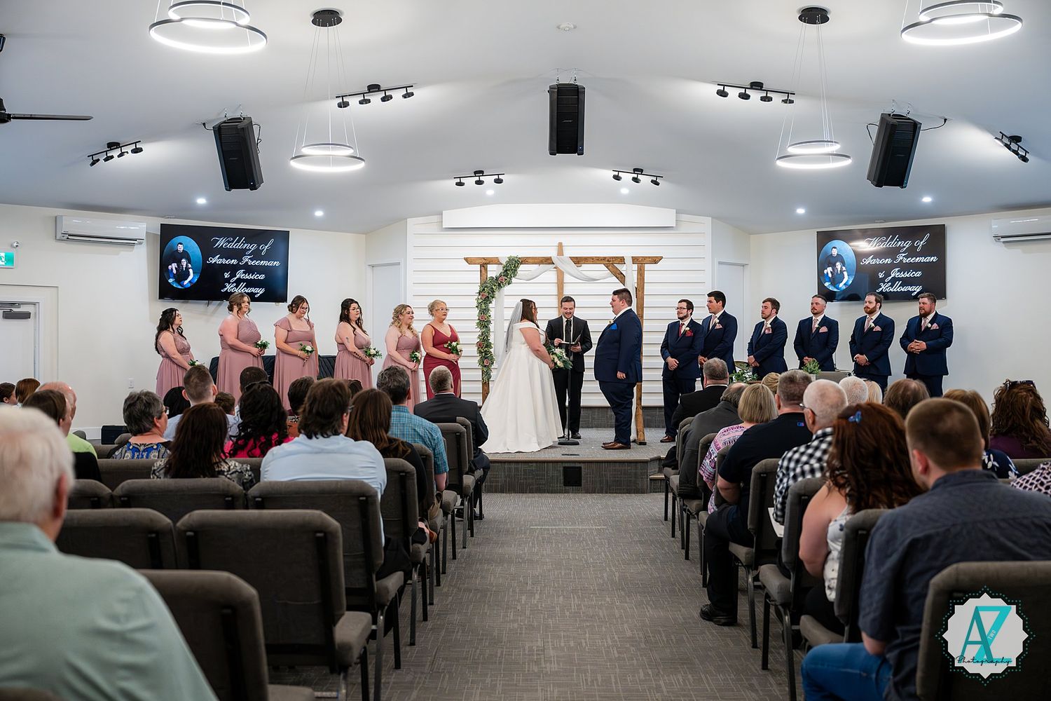 Wedding ceremony taking place in a modern church auditorium with rows of guests seated in chairs.