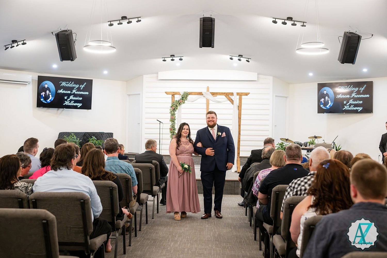 Audience sits in rows of chairs at a business conference or meeting in a bright, modern indoor space.