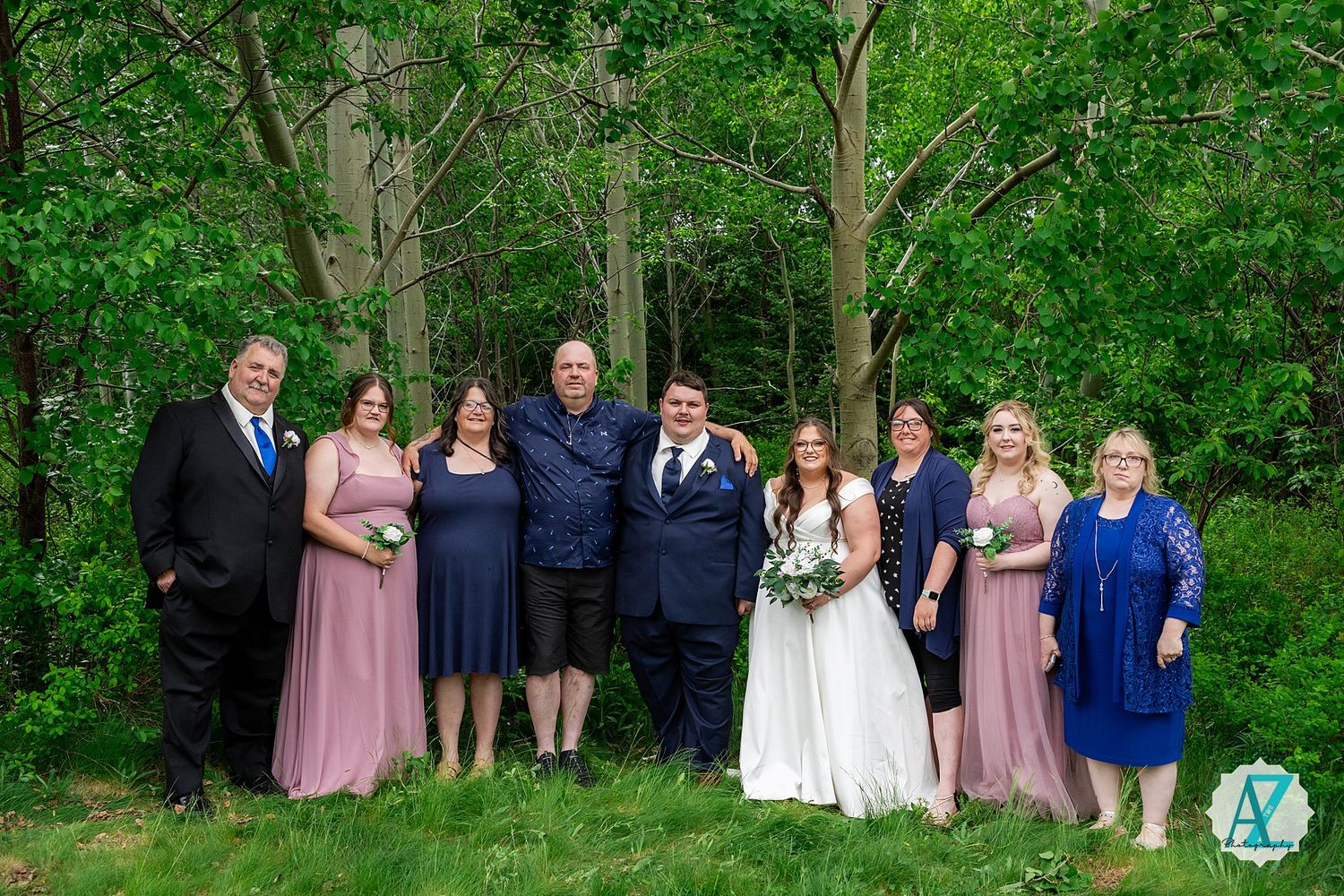 Wedding party poses together for outdoor formal portraits in a lush green forest setting.