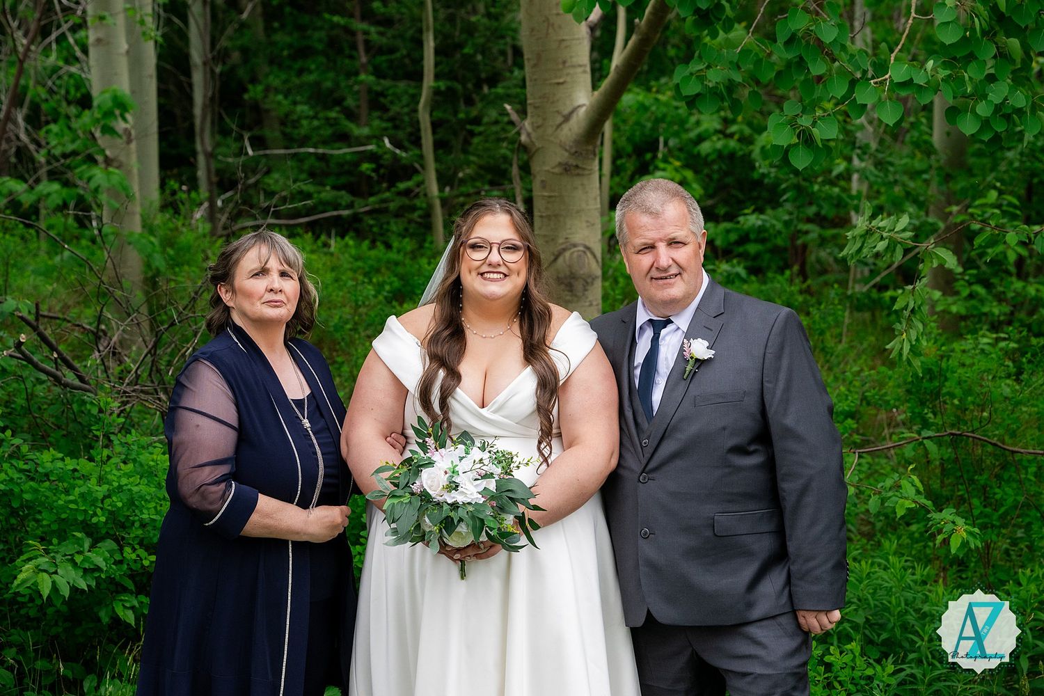 Wedding party poses together against a lush green forest backdrop holding floral bouquets during outdoor ceremony.