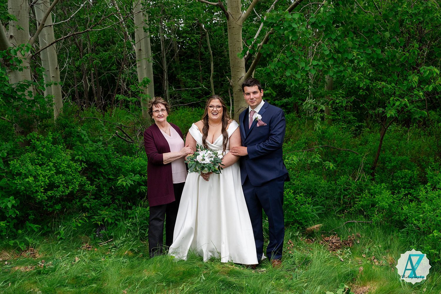 A wedding party poses together in a lush green wooded area on a bright spring day.