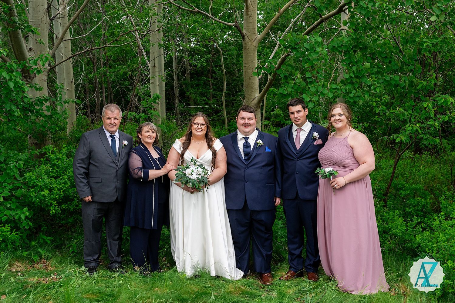 Wedding party standing in front of lush forest background in coordinated navy and pink attire.