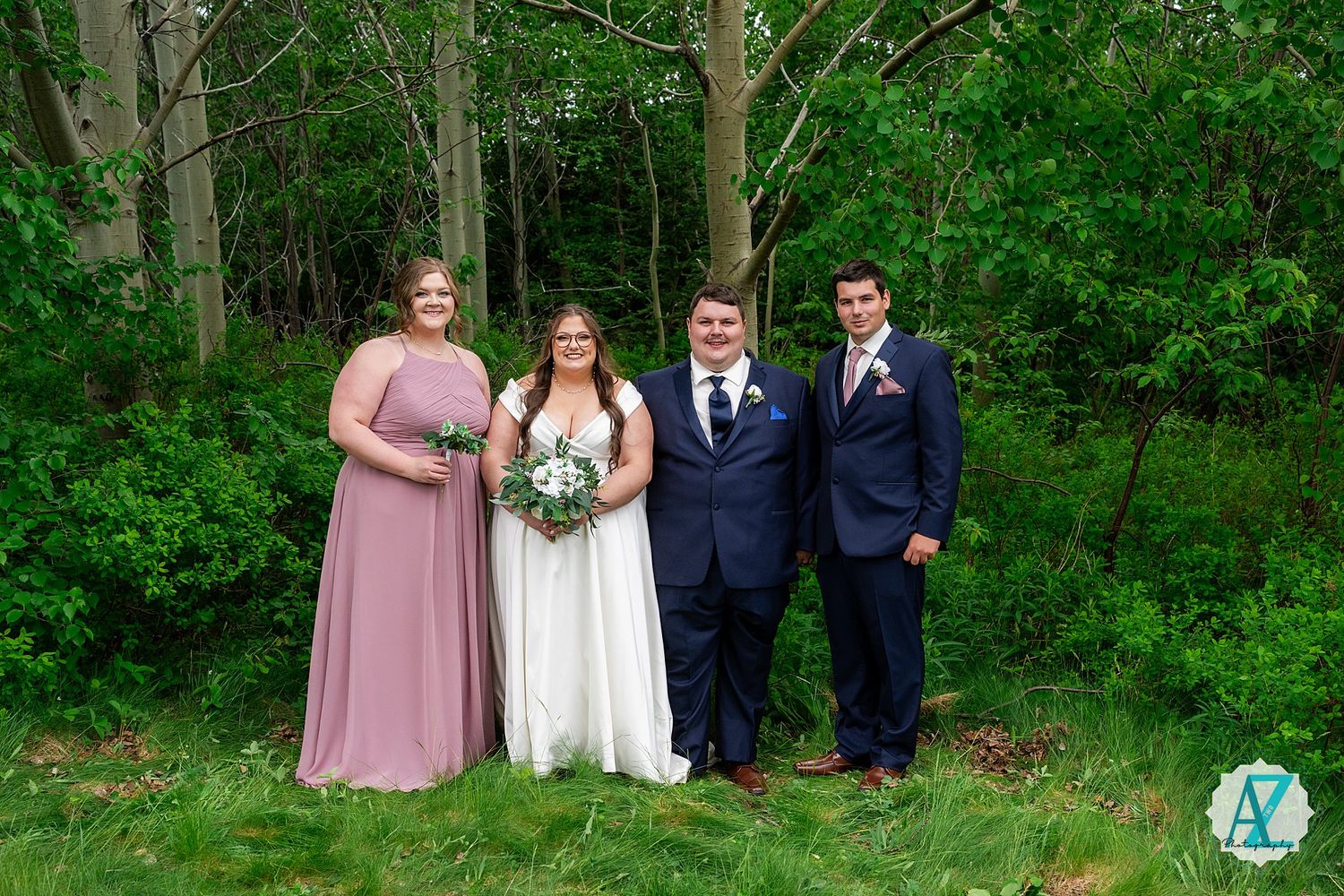 Wedding party of four poses together outdoors against a lush green forest background.