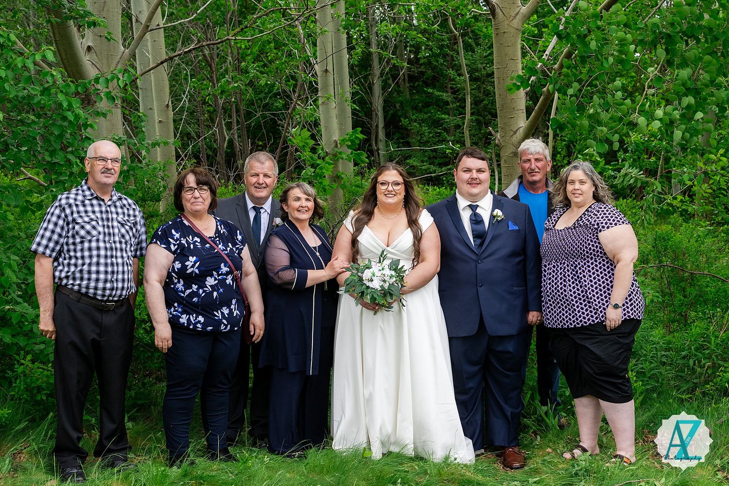 Wedding party group poses outdoors against a lush green forest backdrop in spring.