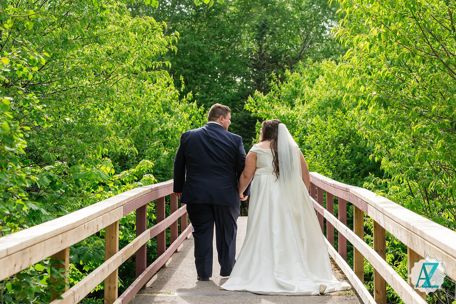 A couple walking away on a wooden bridge surrounded by lush green foliage on their wedding day.