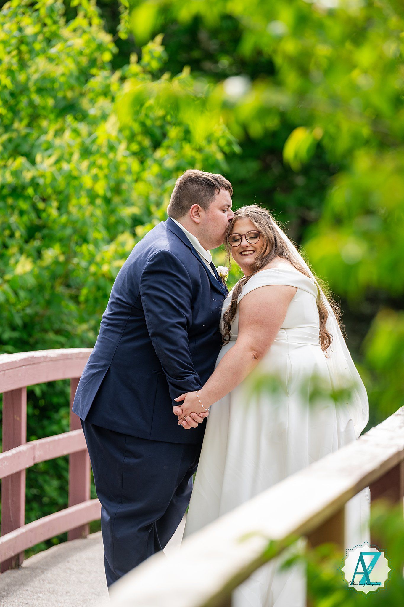 Couple shares an intimate moment on a wooden bridge surrounded by lush green foliage during their wedding photoshoot.