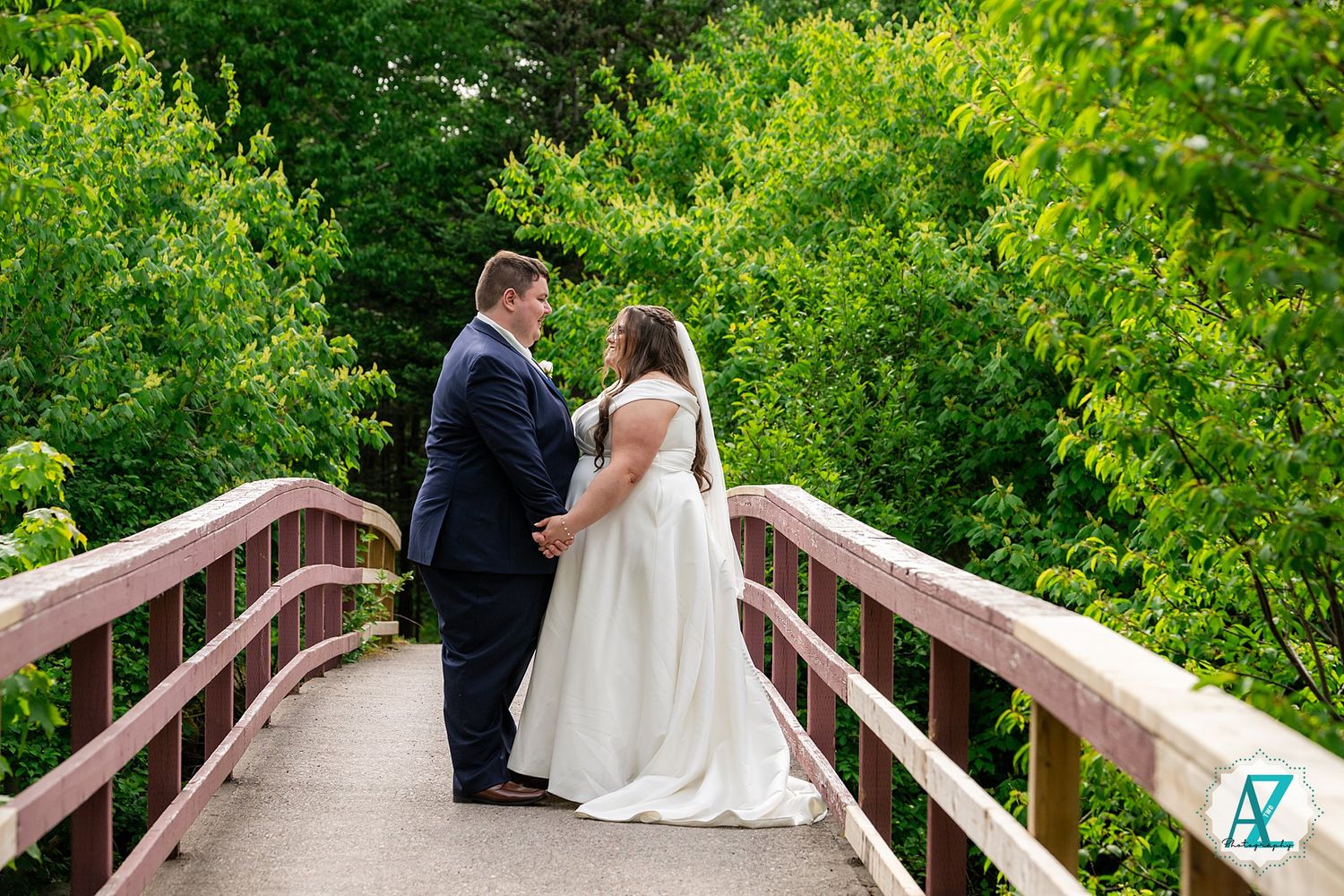 A couple shares an intimate moment on a wooden bridge surrounded by lush green foliage on their wedding day.