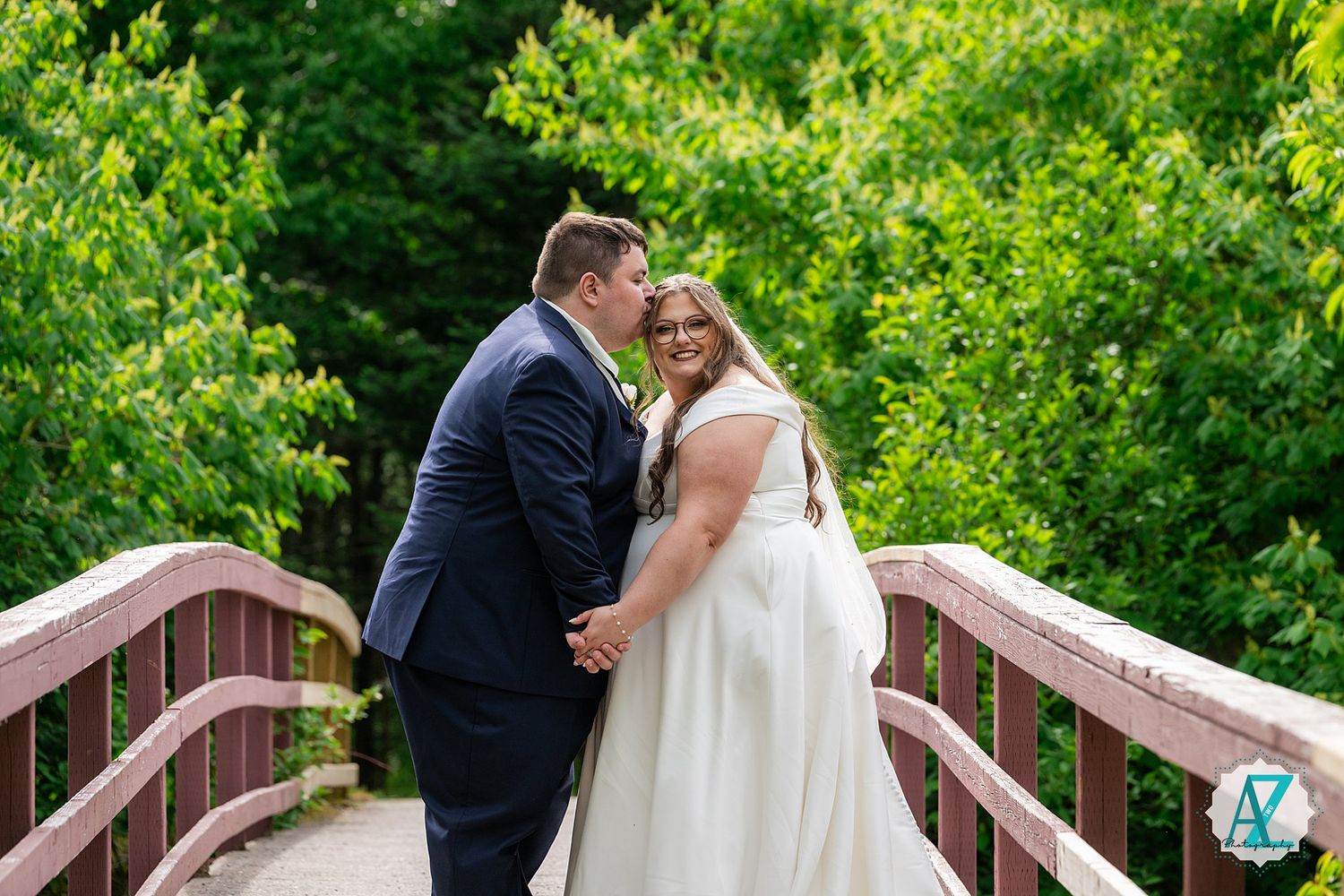 Happy newlyweds sharing a romantic moment on a wooden bridge surrounded by lush green foliage.