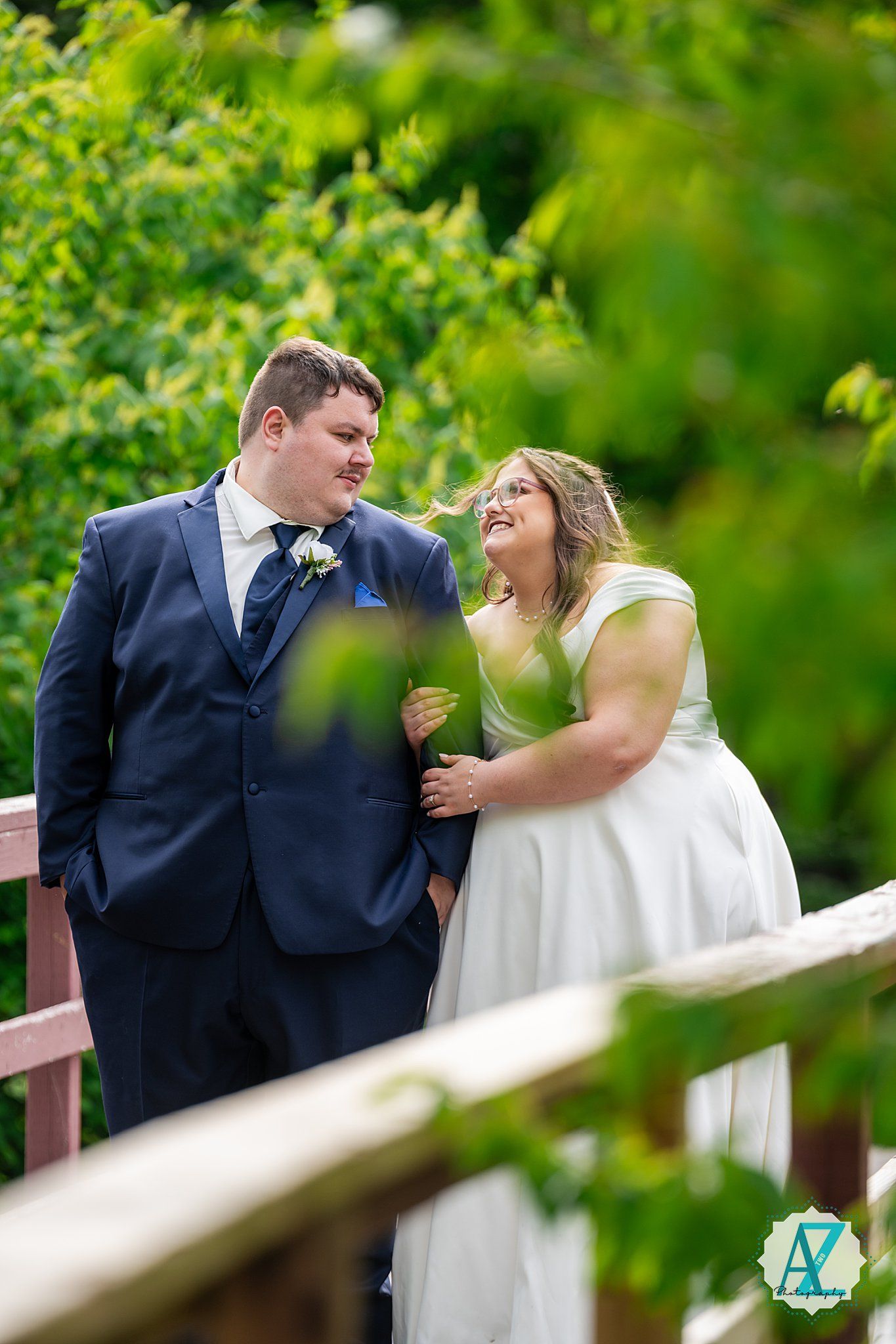 Joyful bride and groom share laughter together on their wedding day surrounded by green foliage.