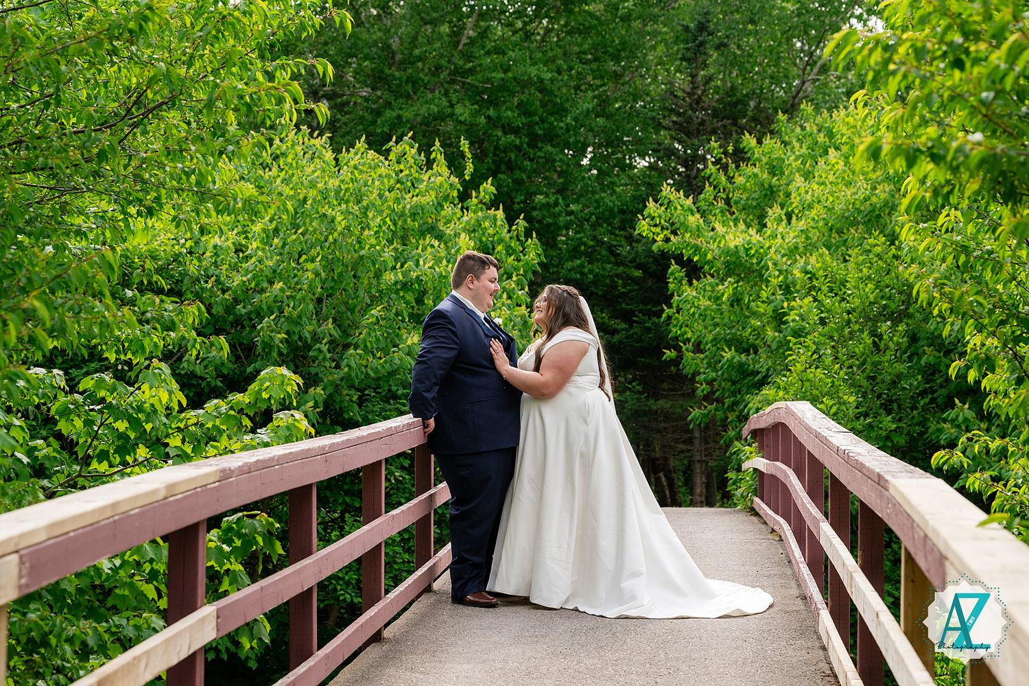 A couple holds hands on a wooden bridge surrounded by lush greenery during an outdoor wedding ceremony.