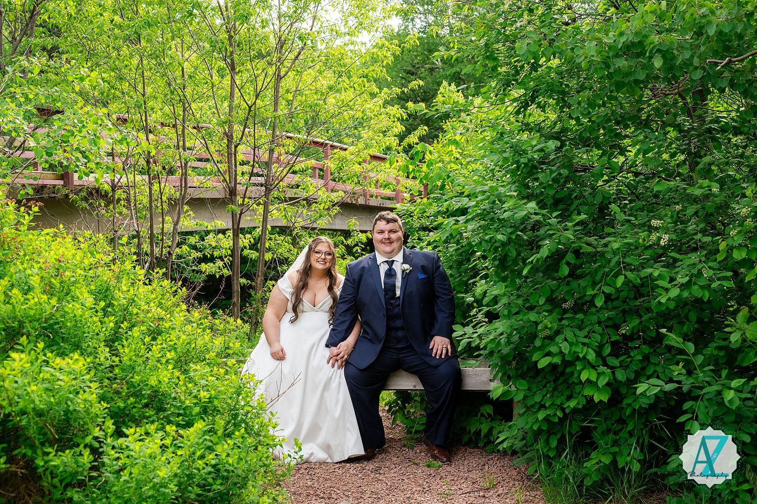 A couple walks hand in hand through a lush garden pathway surrounded by vibrant green foliage on their wedding day.