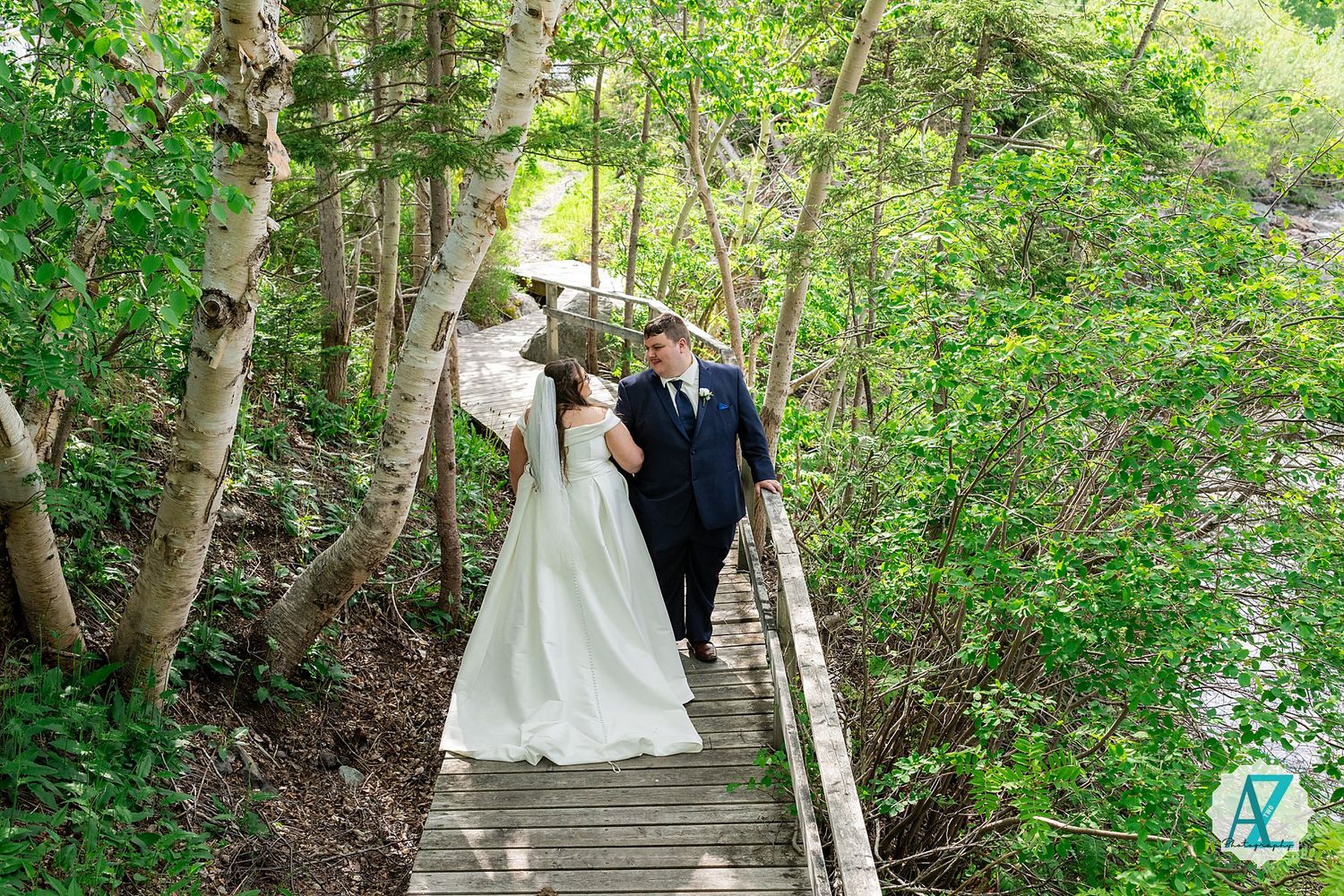 Wedding couple standing on wooden walkway surrounded by lush green forest during an outdoor ceremony.