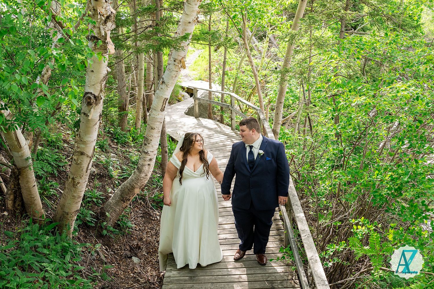 A couple in wedding attire walks together down wooden steps along a lush forest path on their special day.