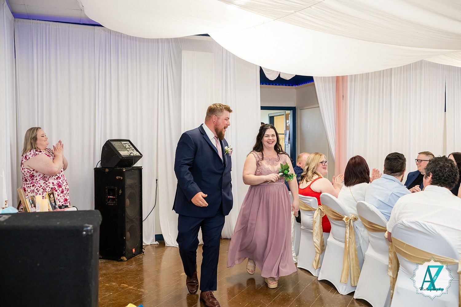 Wedding celebration in decorated reception venue with attendees gathering on dance floor during special moment.