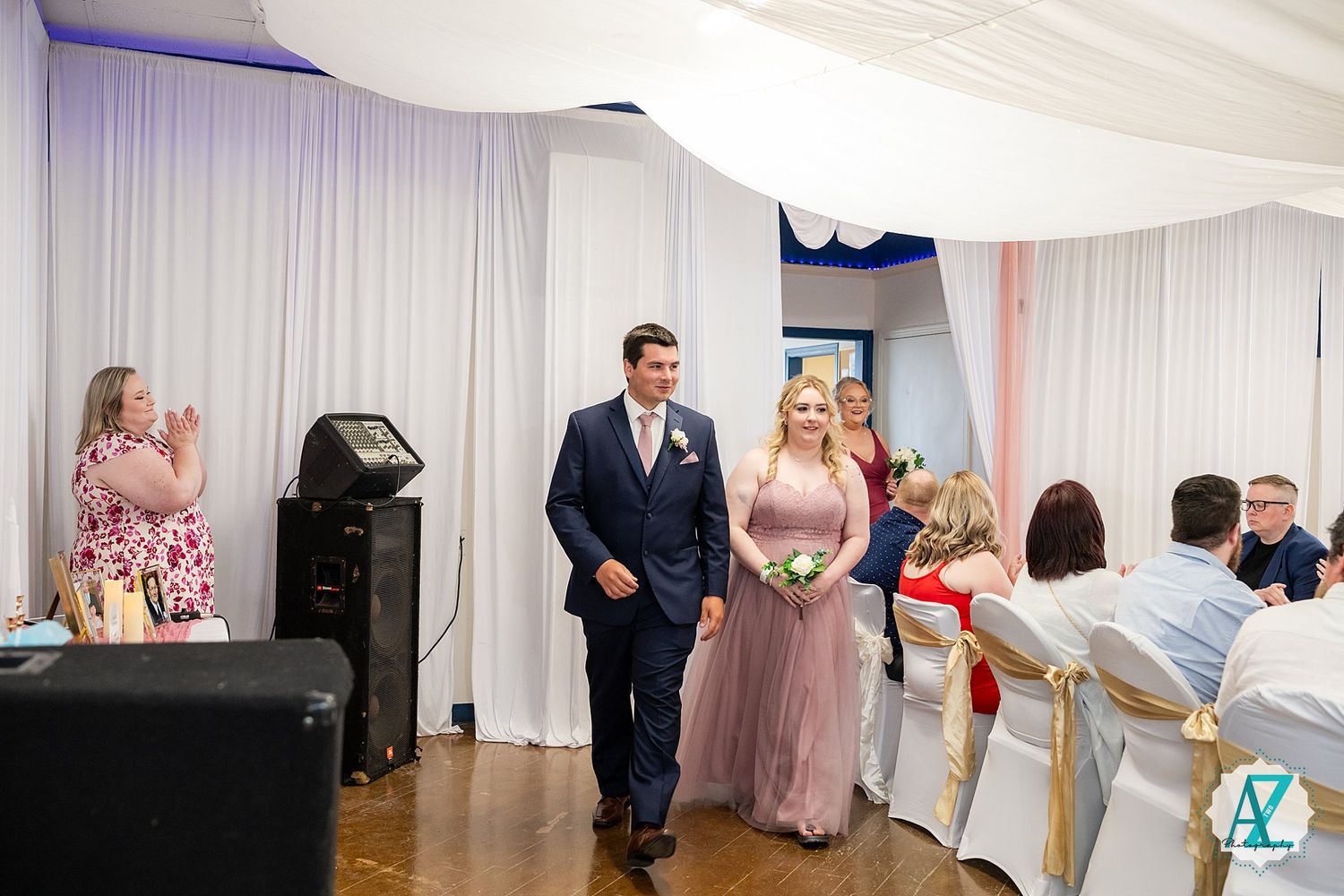Guests in formal attire enter a reception venue decorated with white draping and blue accent lighting for an elegant event.