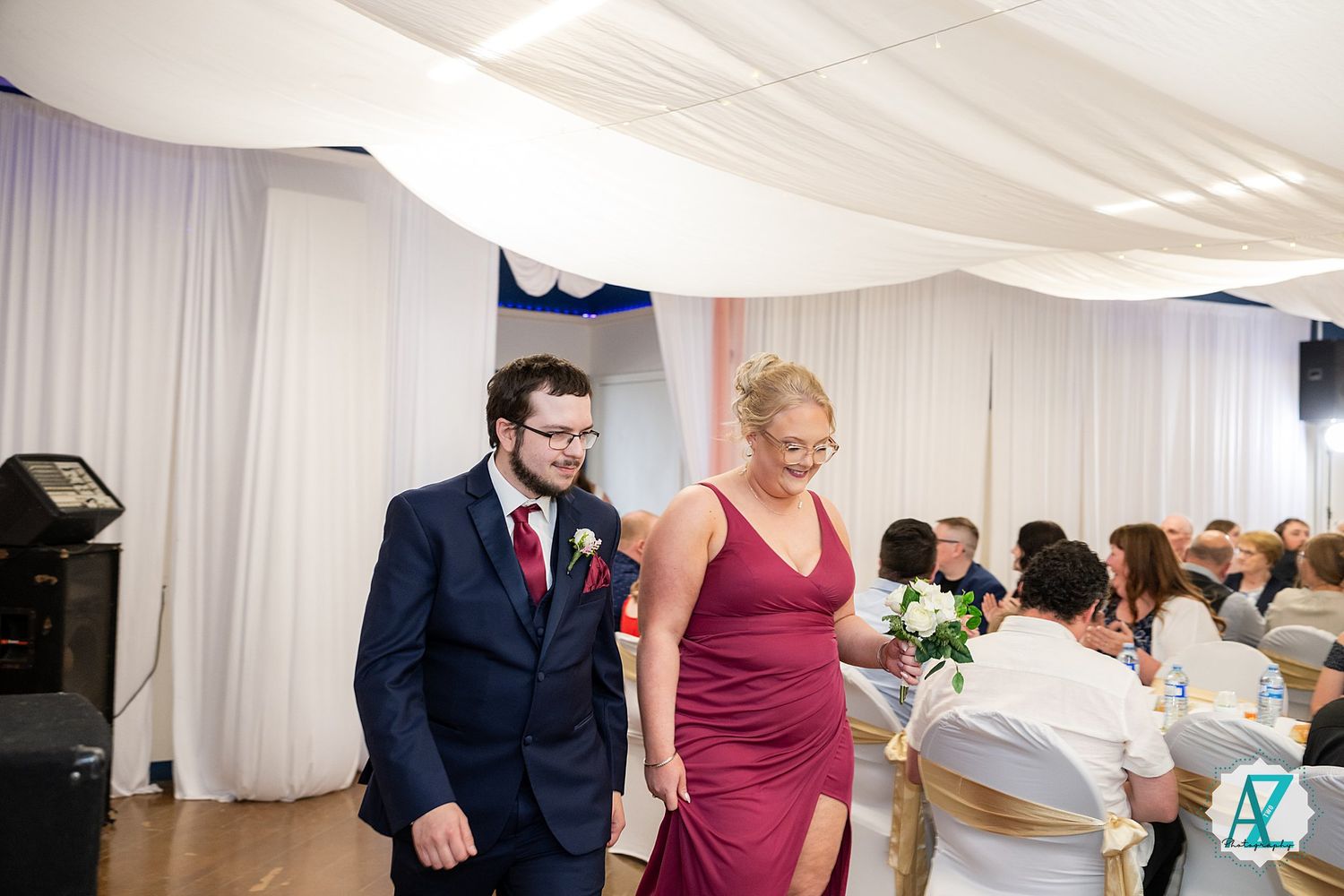 Wedding guests and couple socialize and dance at their reception inside a white draped tent.