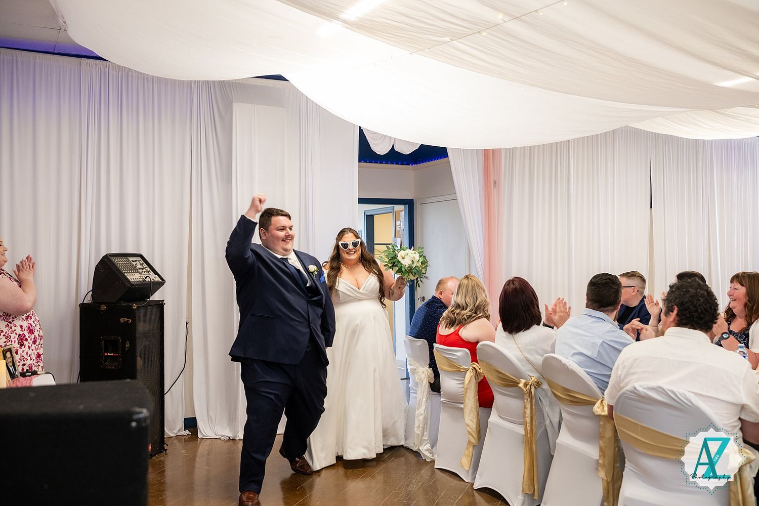 Newlyweds celebrate with their arms raised in joyful victory at their indoor wedding reception.