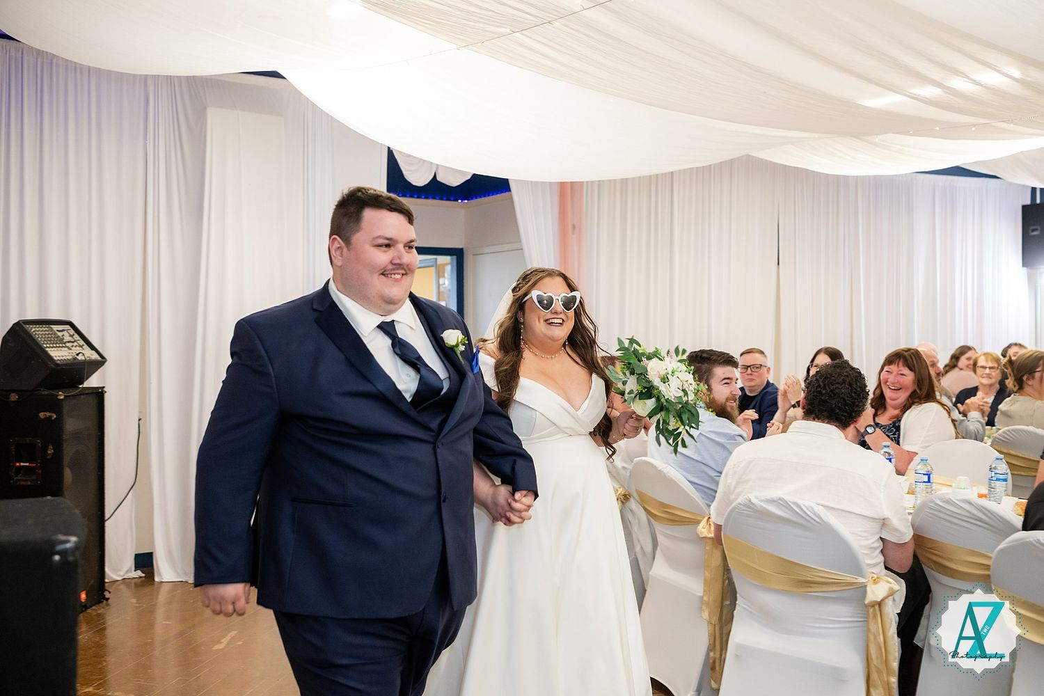 Wedding guests enjoying a dance party on the reception dance floor with white drapes and chandeliers overhead.