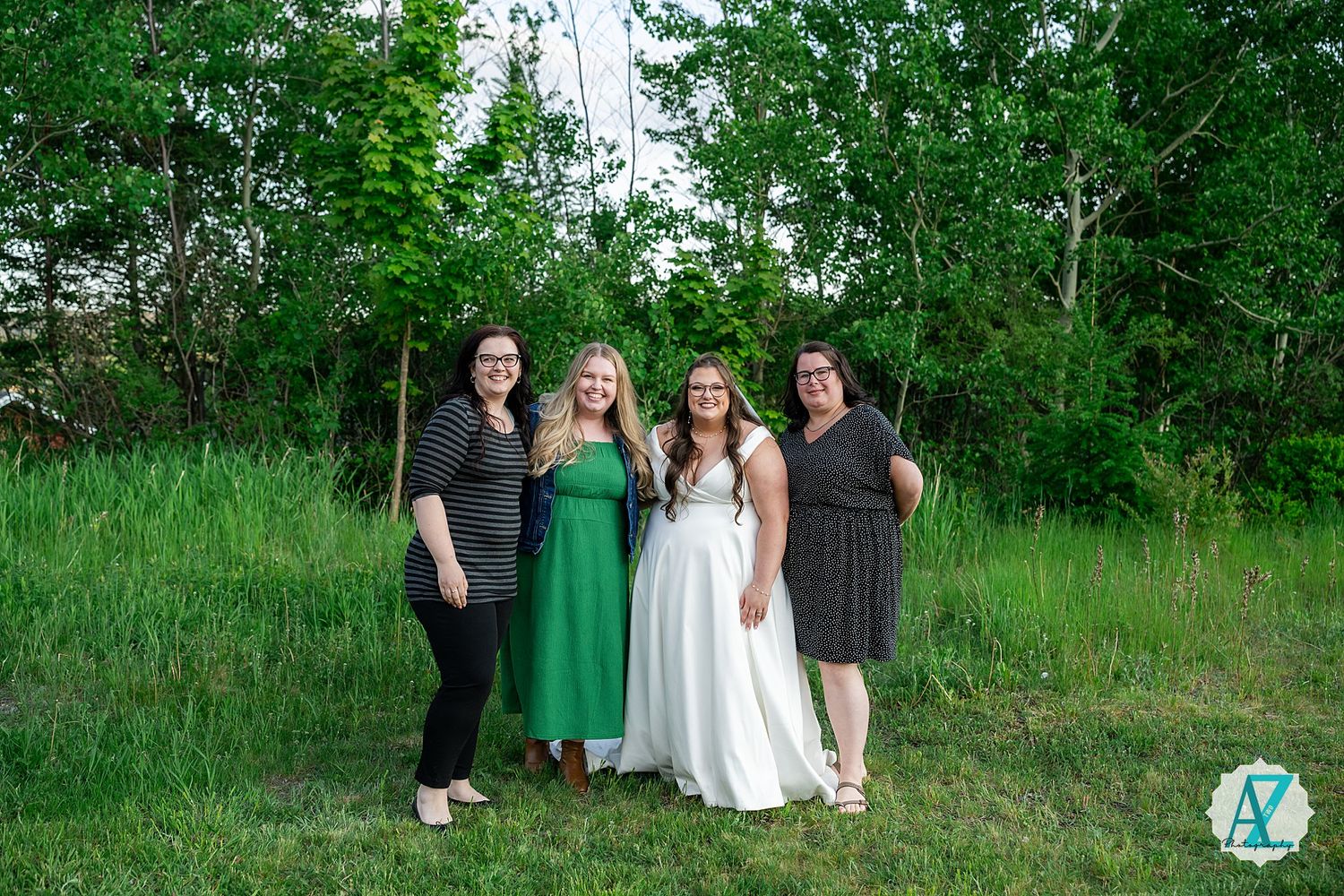 A group of four people pose together on grassy terrain with lush green trees in the background.