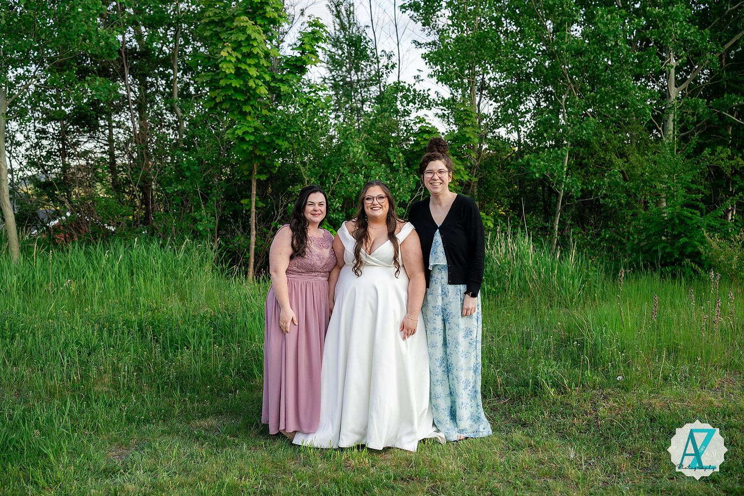 A wedding party stands together in an outdoor setting with lush green foliage and natural surroundings.