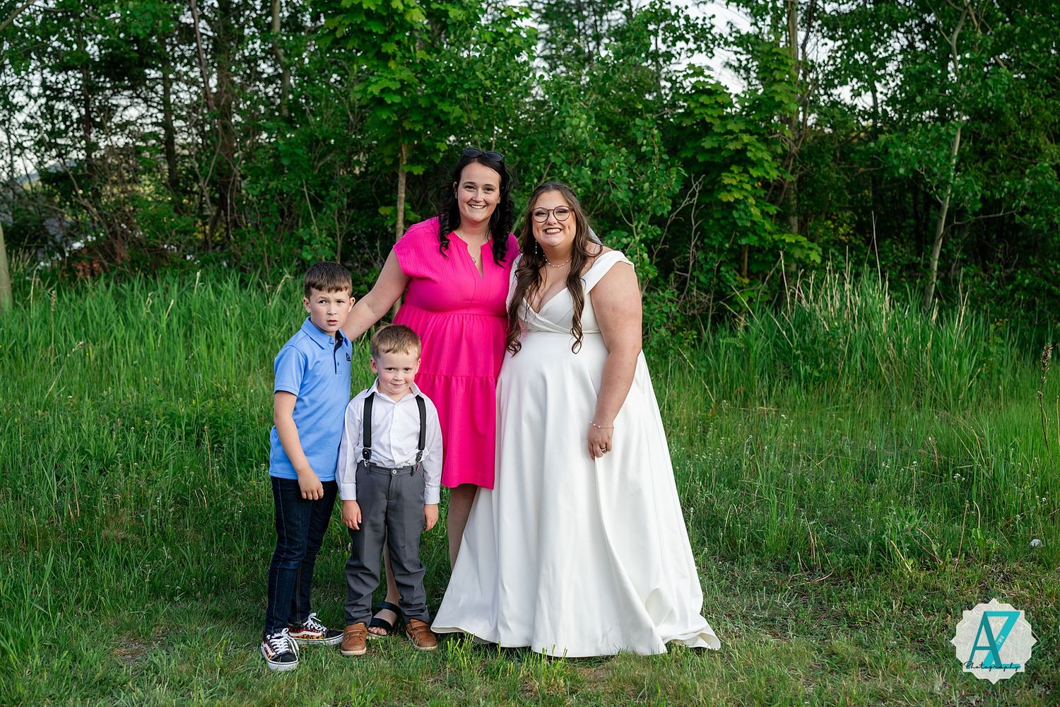 A group of people pose together on grassy terrain with green trees and foliage in the background.