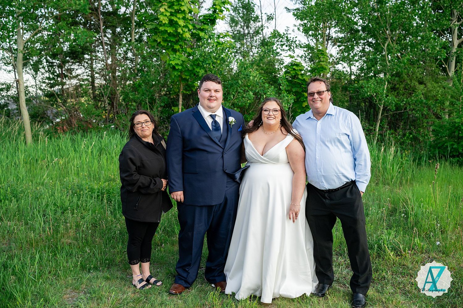 A wedding party stands together in various poses outdoors against a lush green forest background.