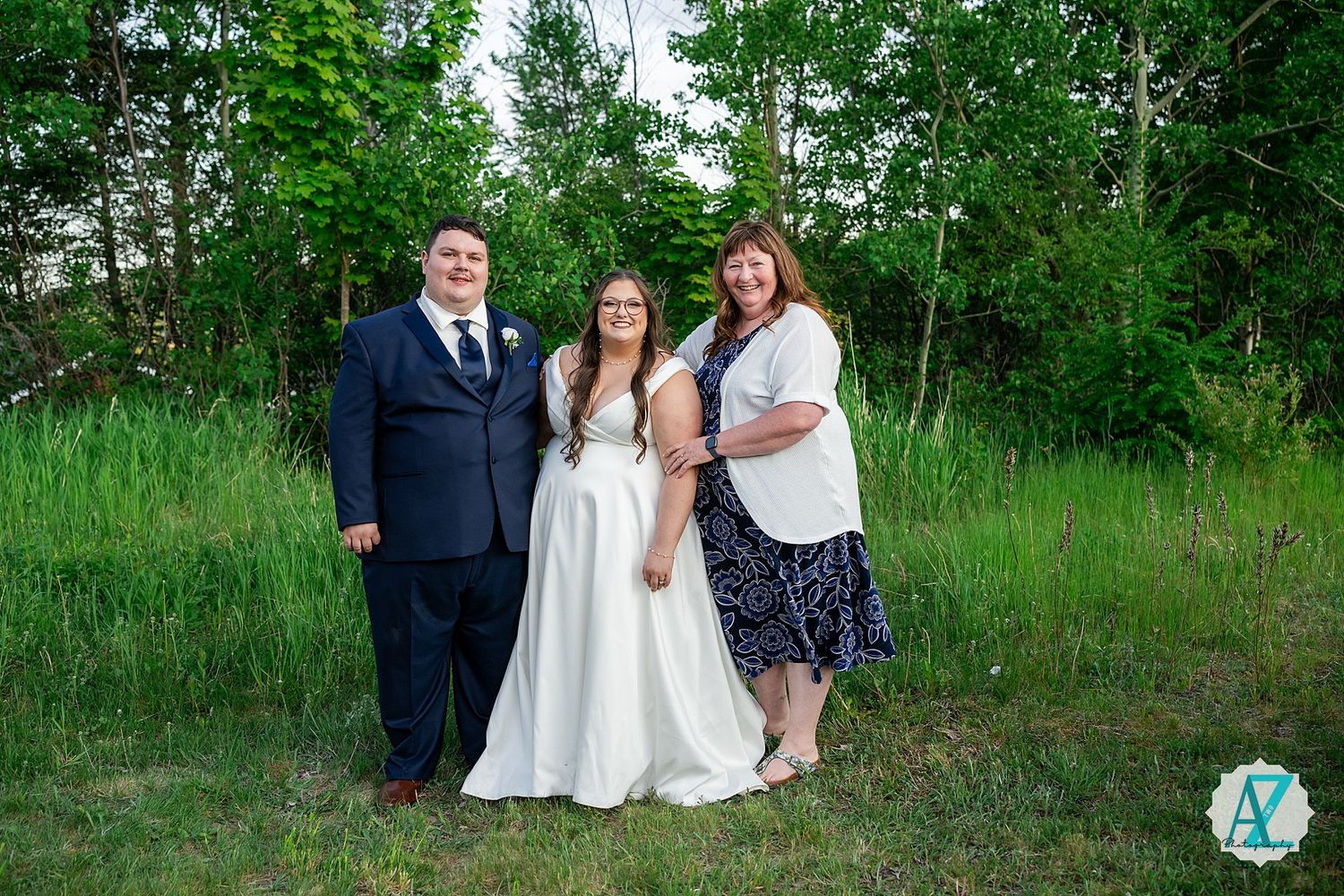 Wedding party poses in lush green field for outdoor summer portraits.
