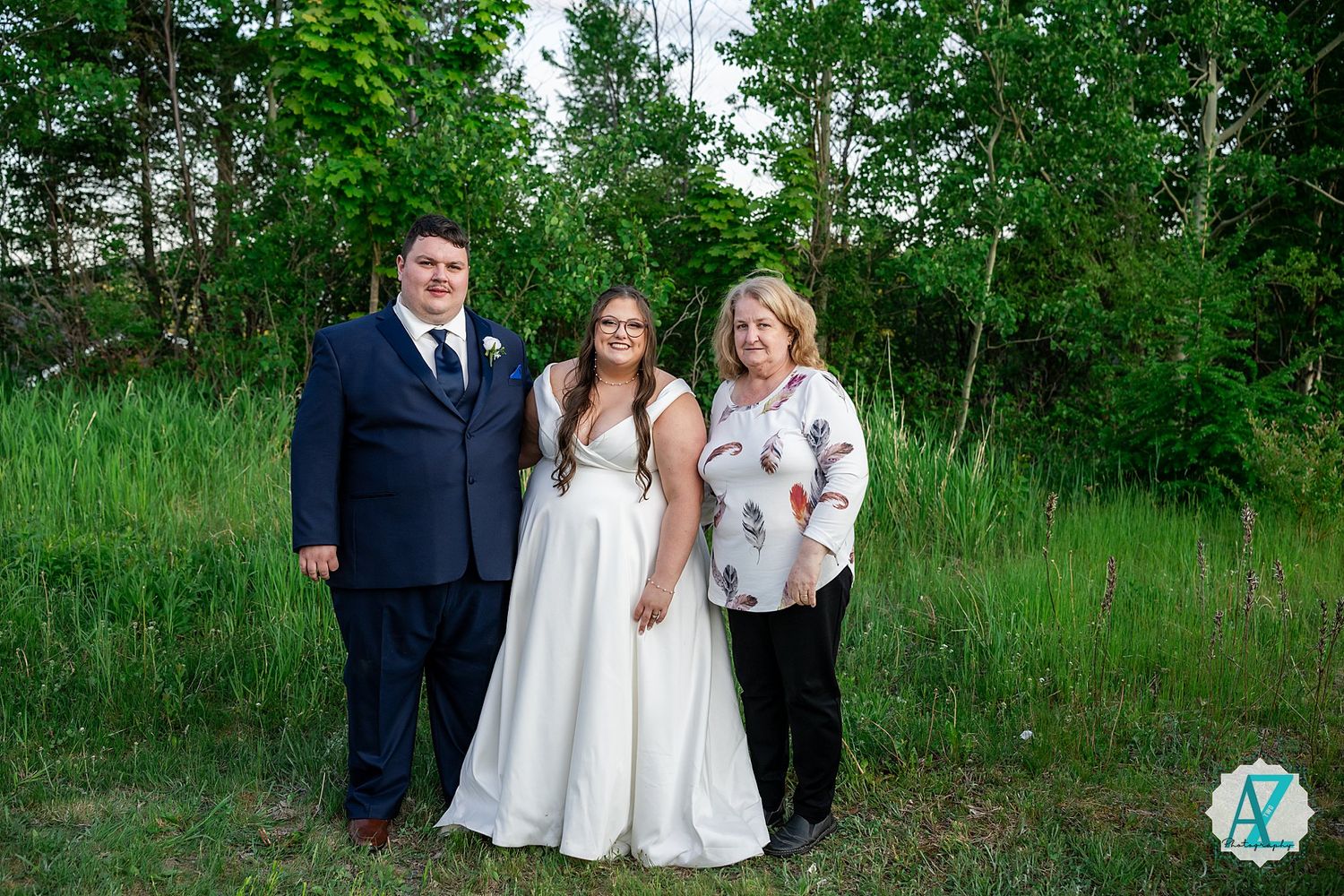 Wedding party stands on a green hillside in formal attire during summer celebration.