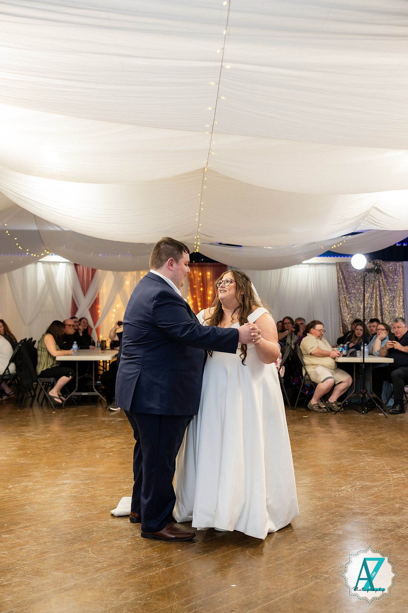 Wedding guests performing a group dance moves sequence at a reception party in a white tented venue.