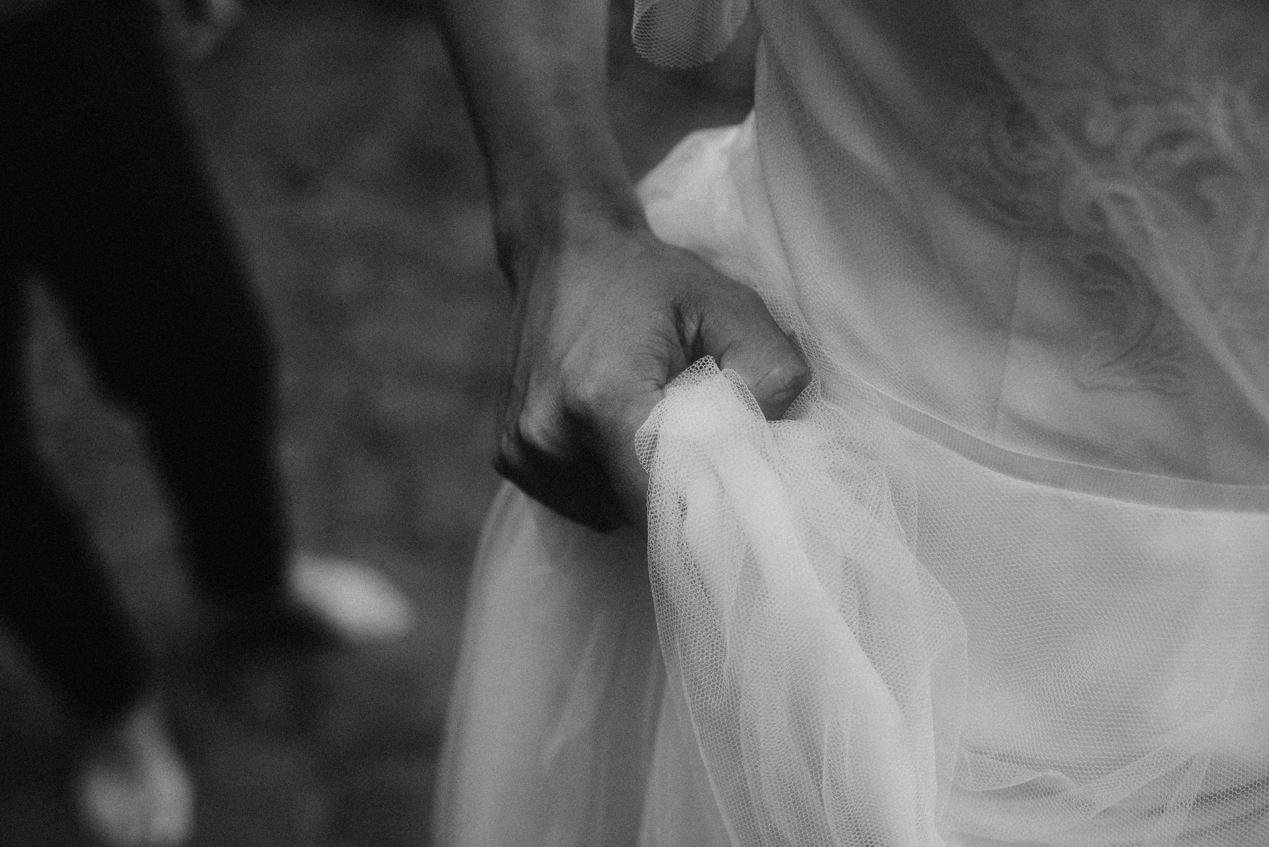 Close-up black and white detail of hands adjusting the delicate fabric and lace of a wedding dress.