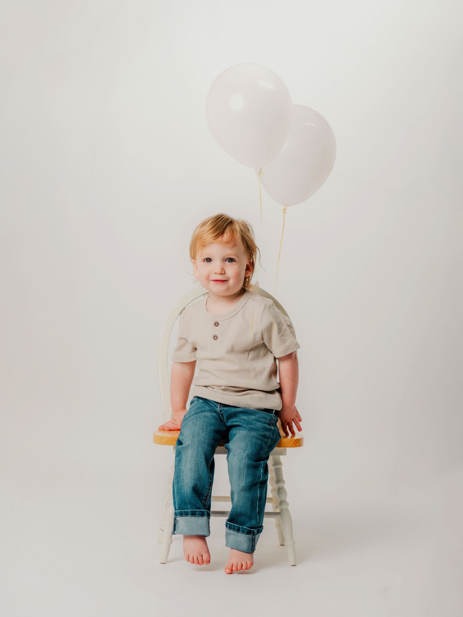 A small child wearing a floral outfit sits happily in a decorative white boat prop with a fishing rod.