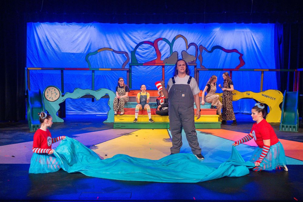 A colorful stage performance with performers in a nautical-themed set with blue lighting and whimsical fabric waves.