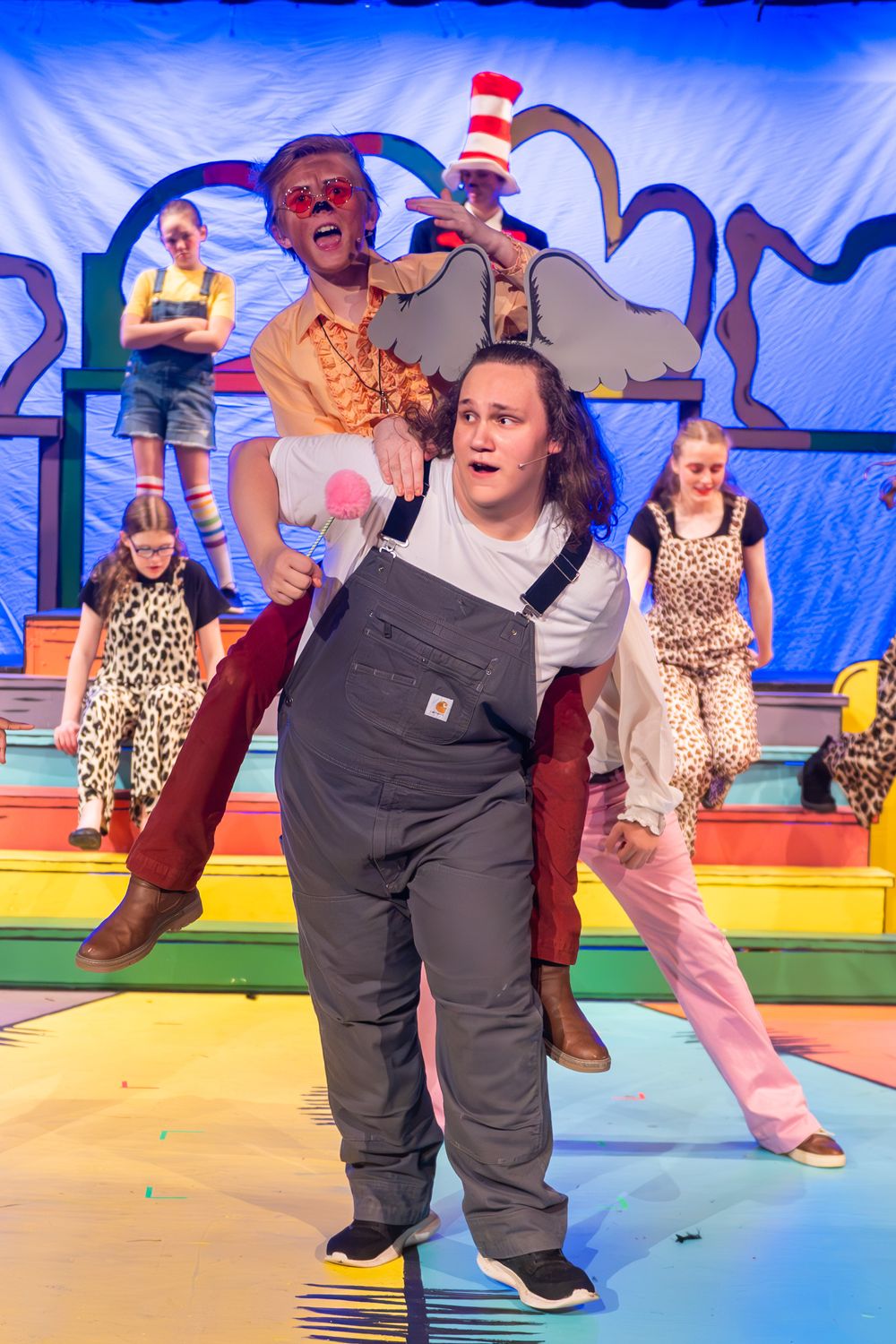 Actors perform in a colorful stage production of Seussical the Musical with whimsical costumes and rainbow set design.